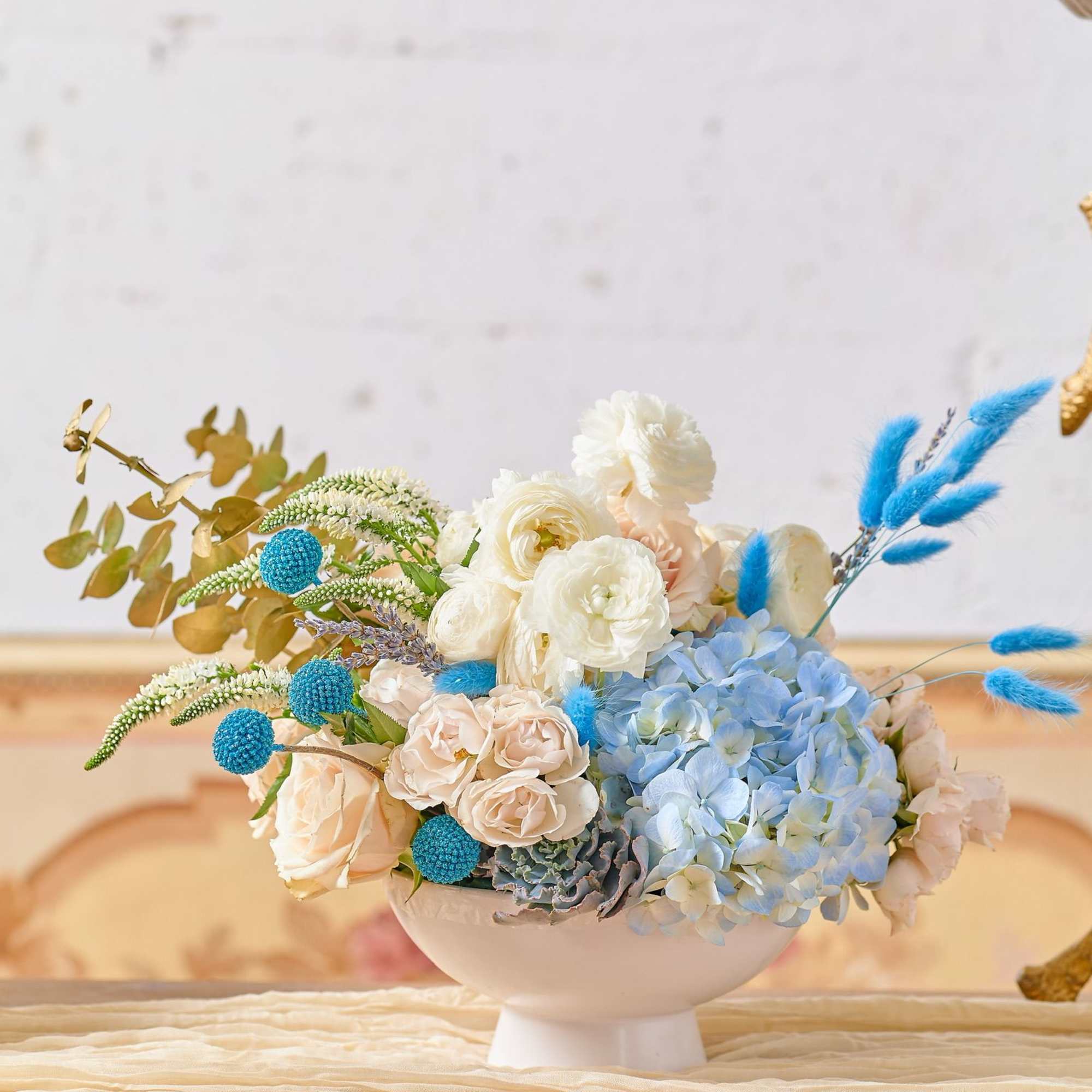 Pastel floral arrangement in a white pedestal bowl with blue accents