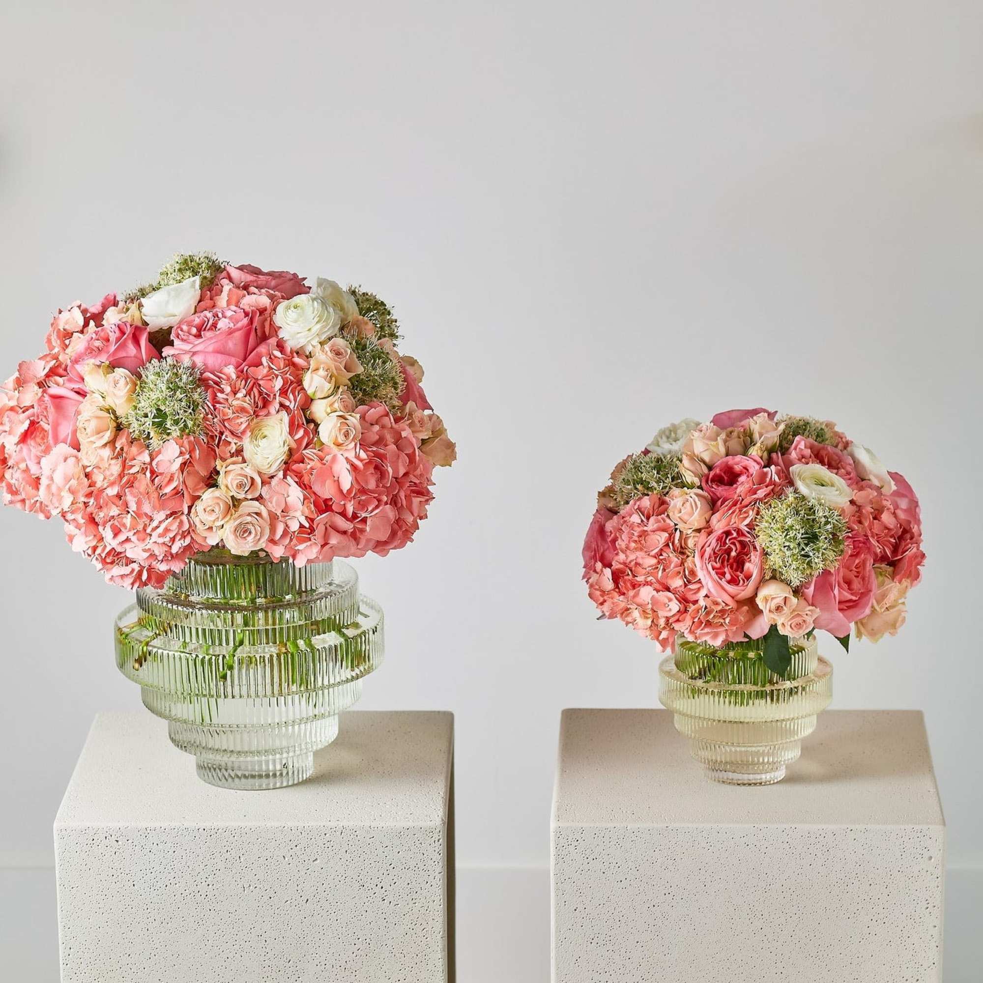 Two pink floral arrangements in ribbed glass vases on white pedestals