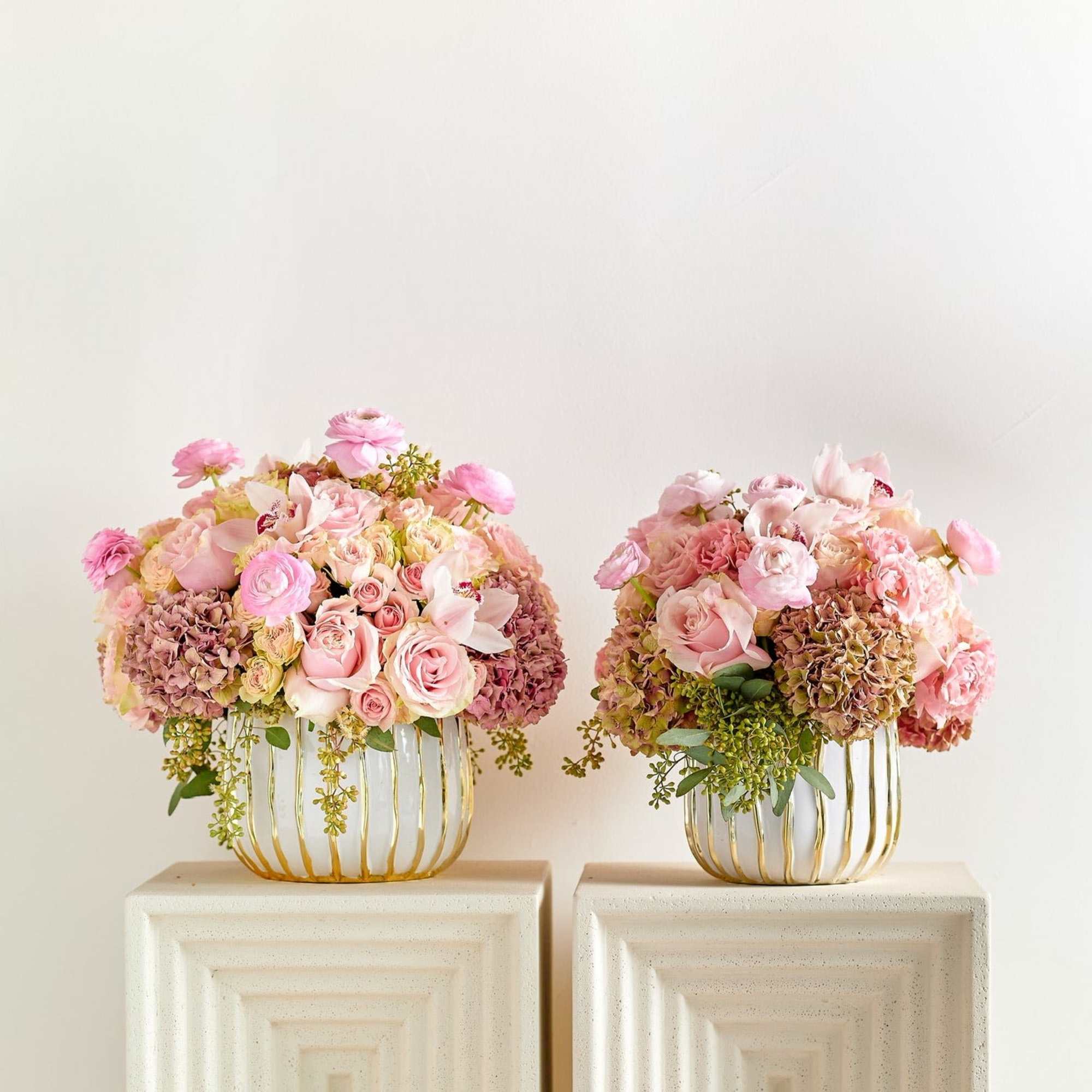 Two pink floral arrangements in gold wire vases on pedestals
