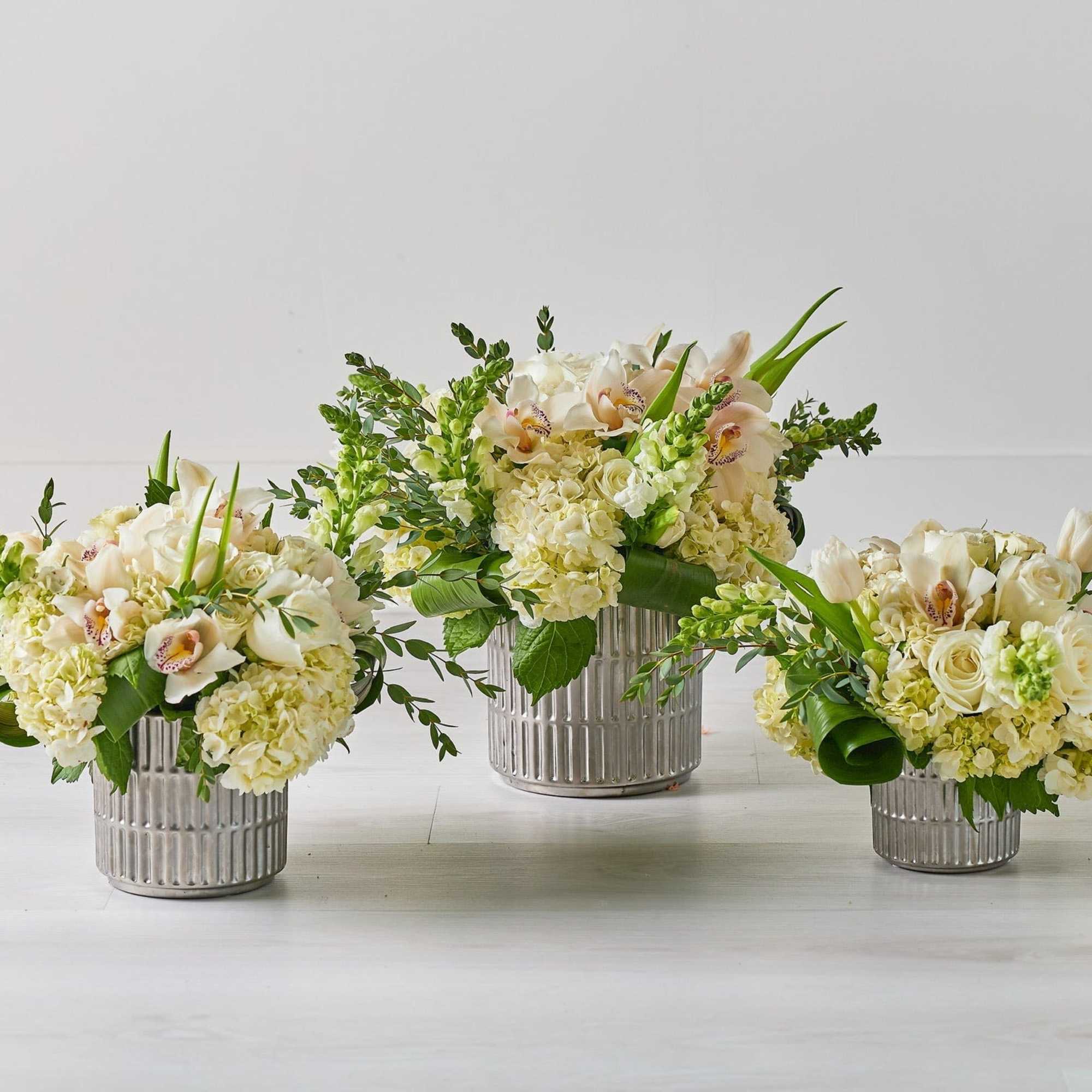 Three cream floral arrangements in ribbed silver vases