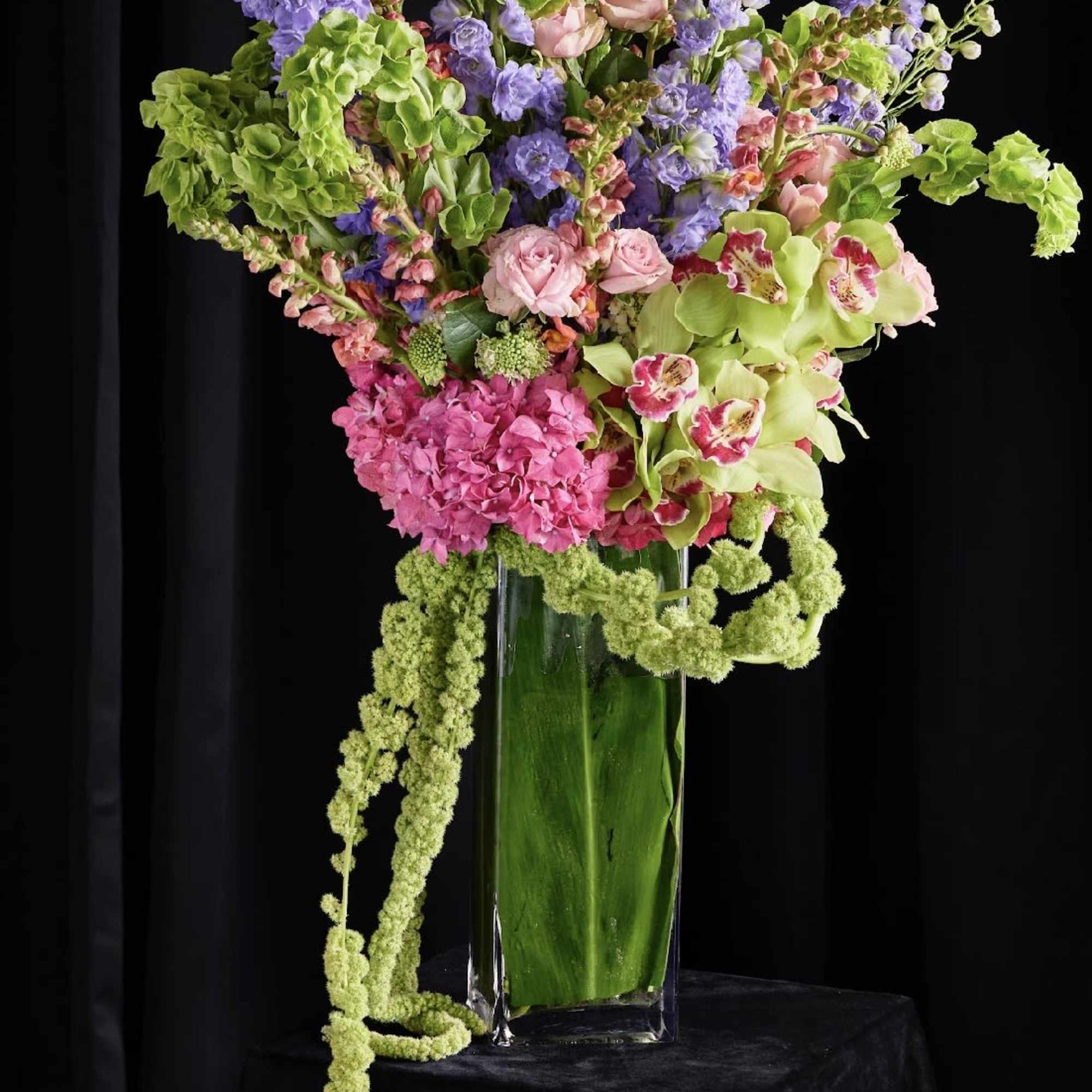 Tall mixed floral arrangement in a clear glass vase with pink, purple, and green blooms