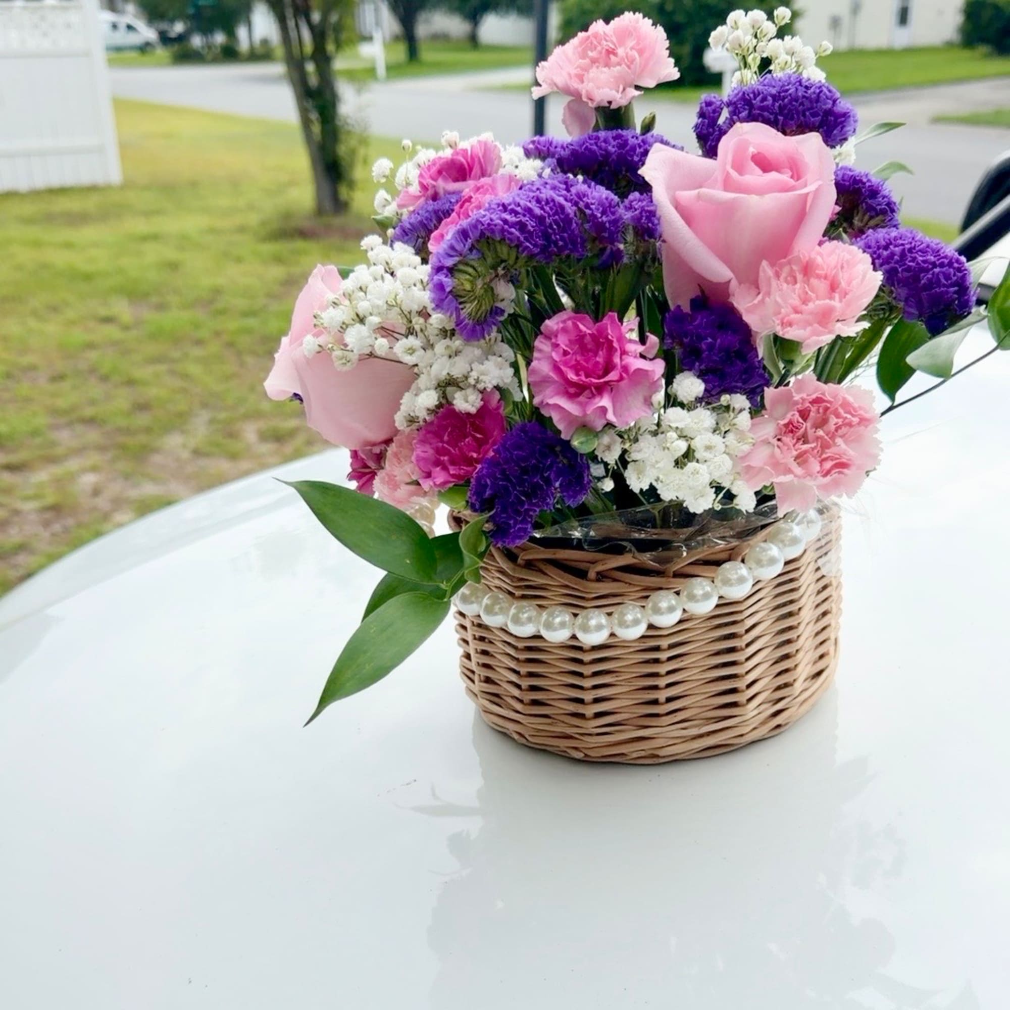 Pink and purple flower arrangement in a wicker basket with pearl trim