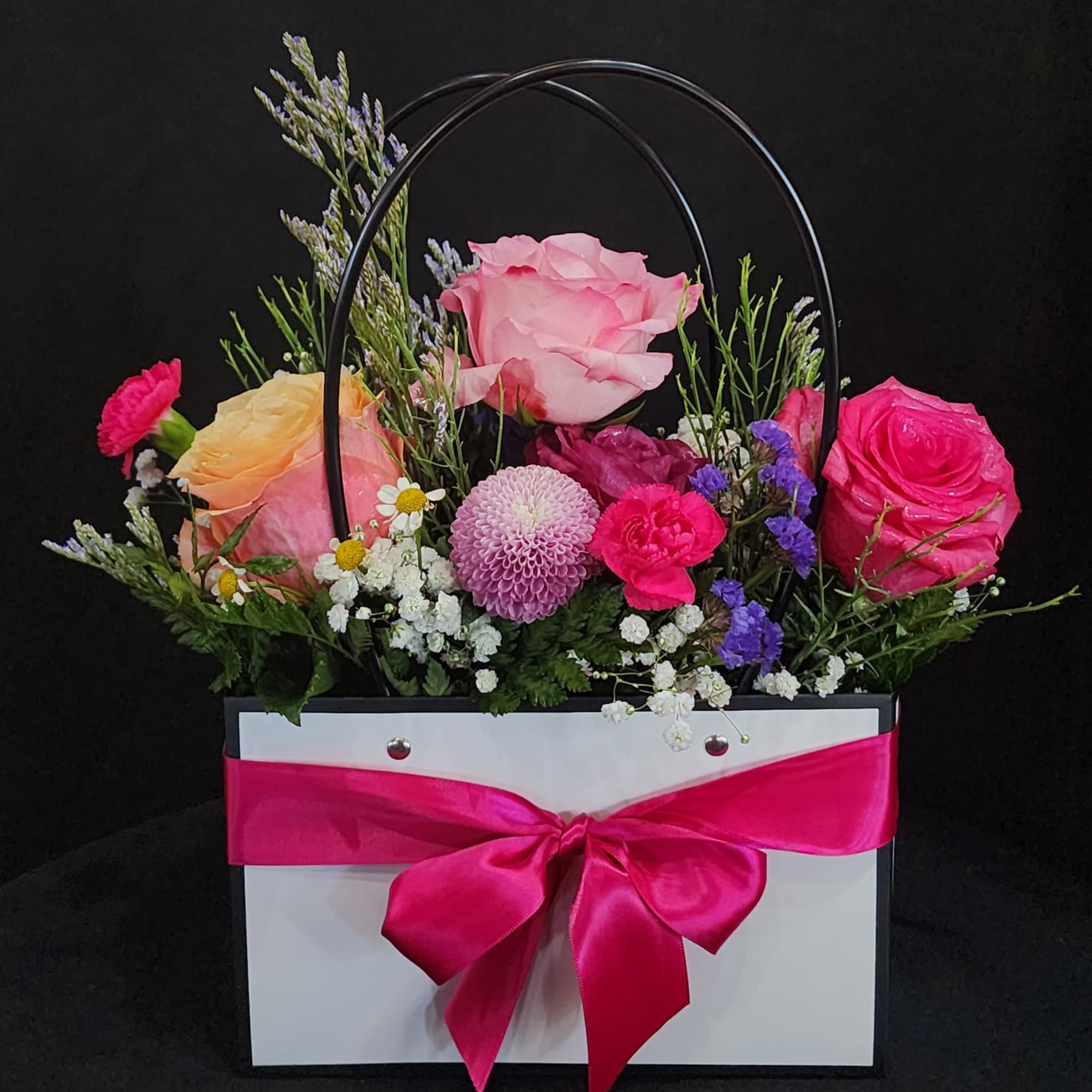 Mixed flower arrangement in a white gift bag with a pink ribbon