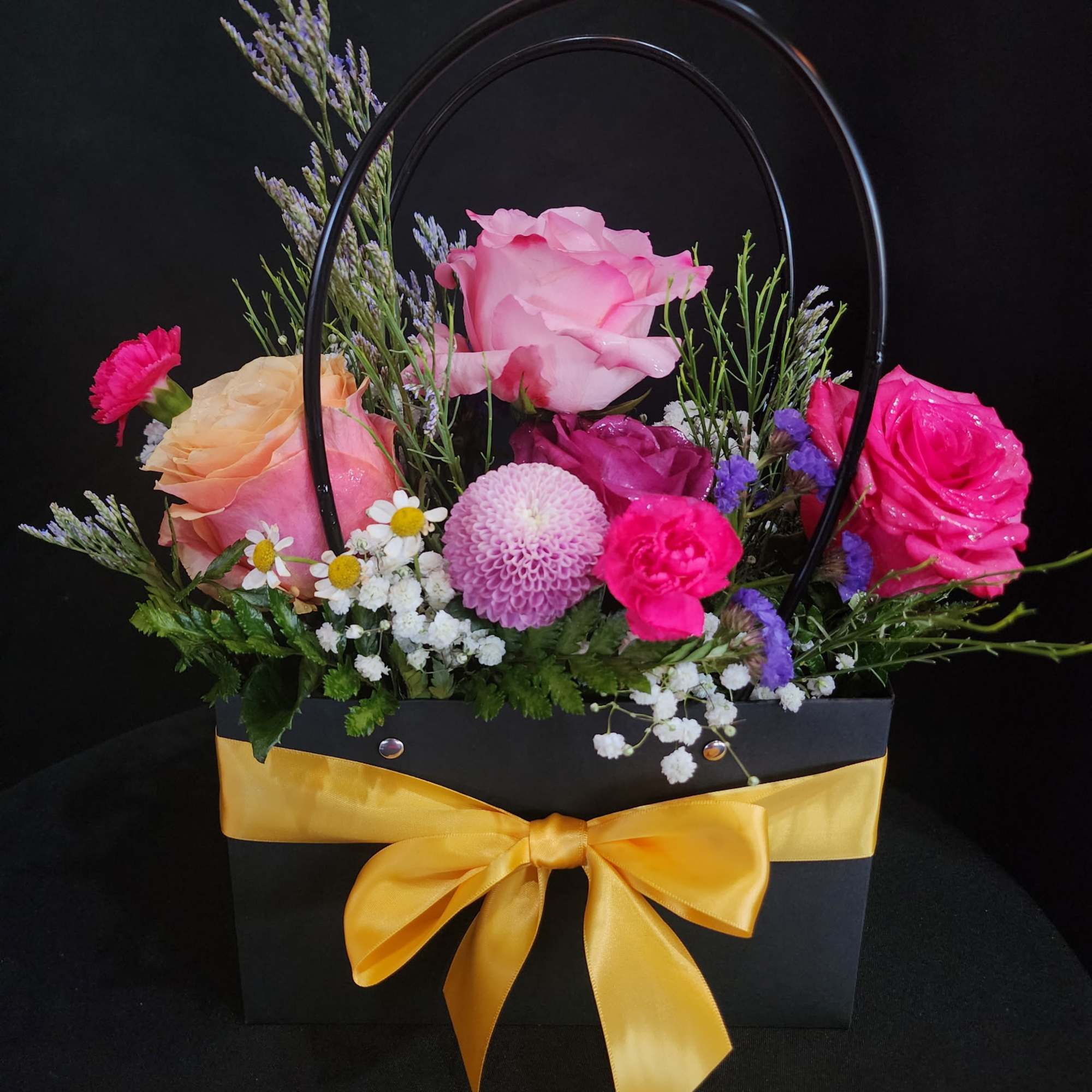 Mixed pink and purple flower arrangement in a black gift bag with a yellow ribbon
