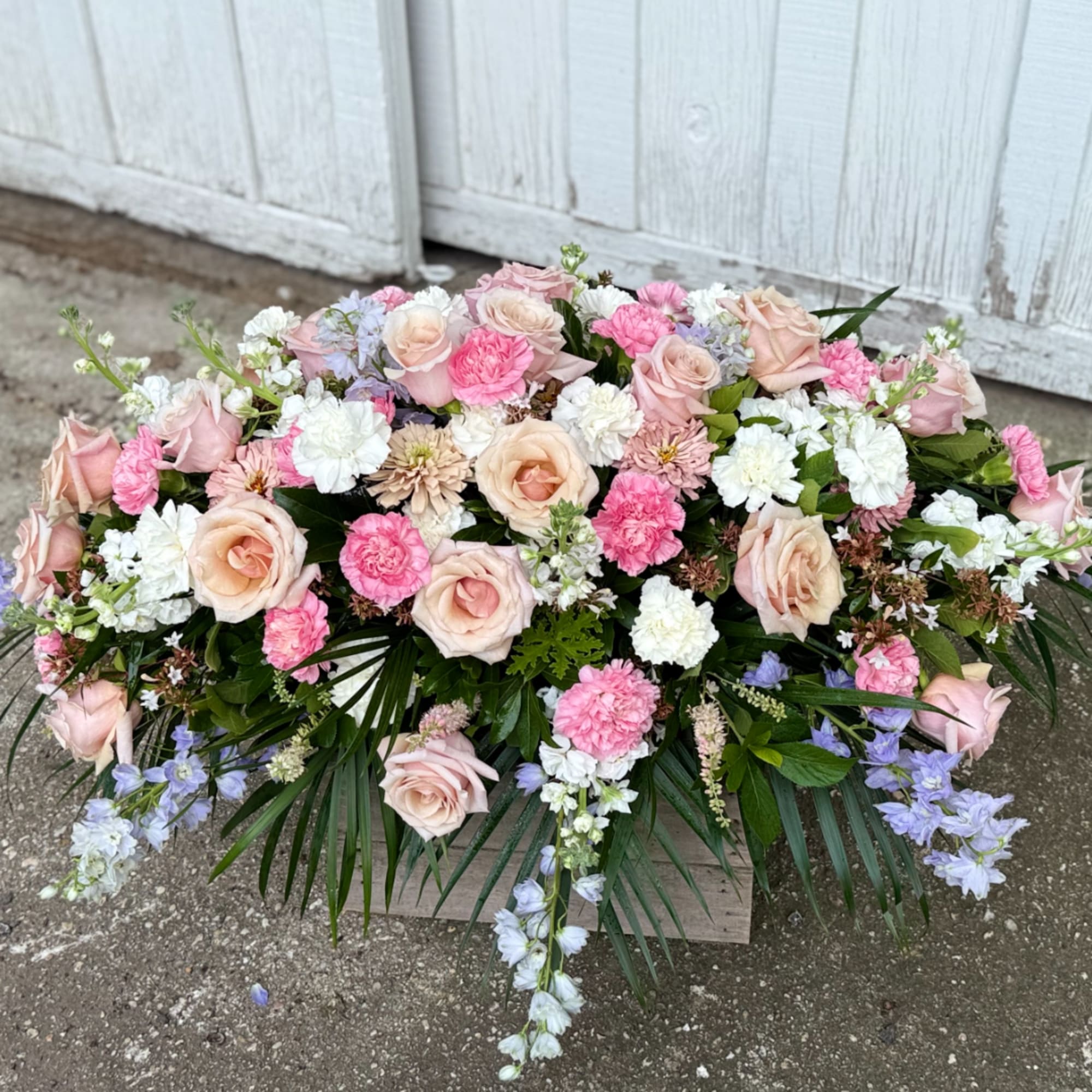 Large pastel floral arrangement with roses, carnations, and blue flowers in a wooden box