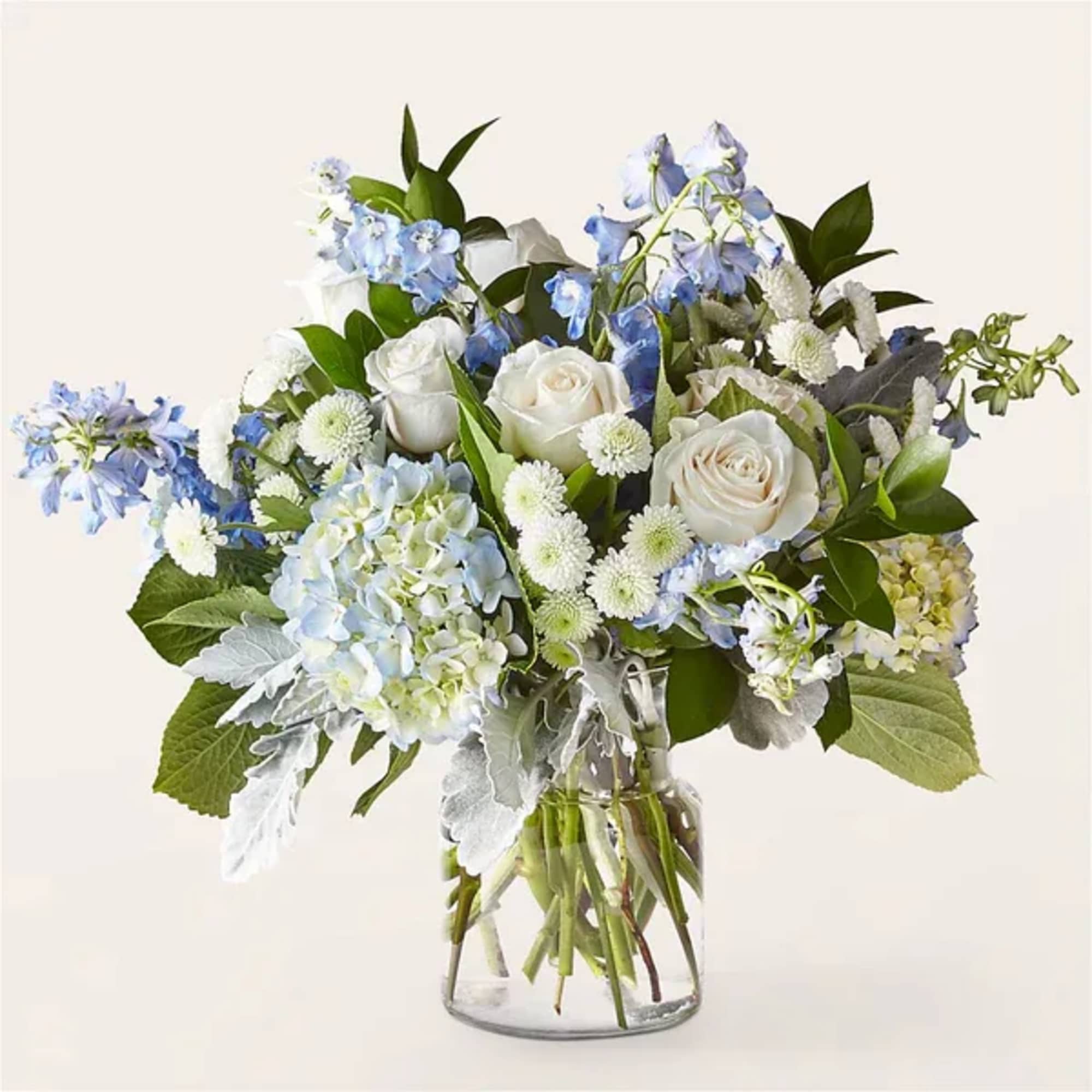 Arrangement of white roses, blue hydrangeas, and white mums in a clear glass vase