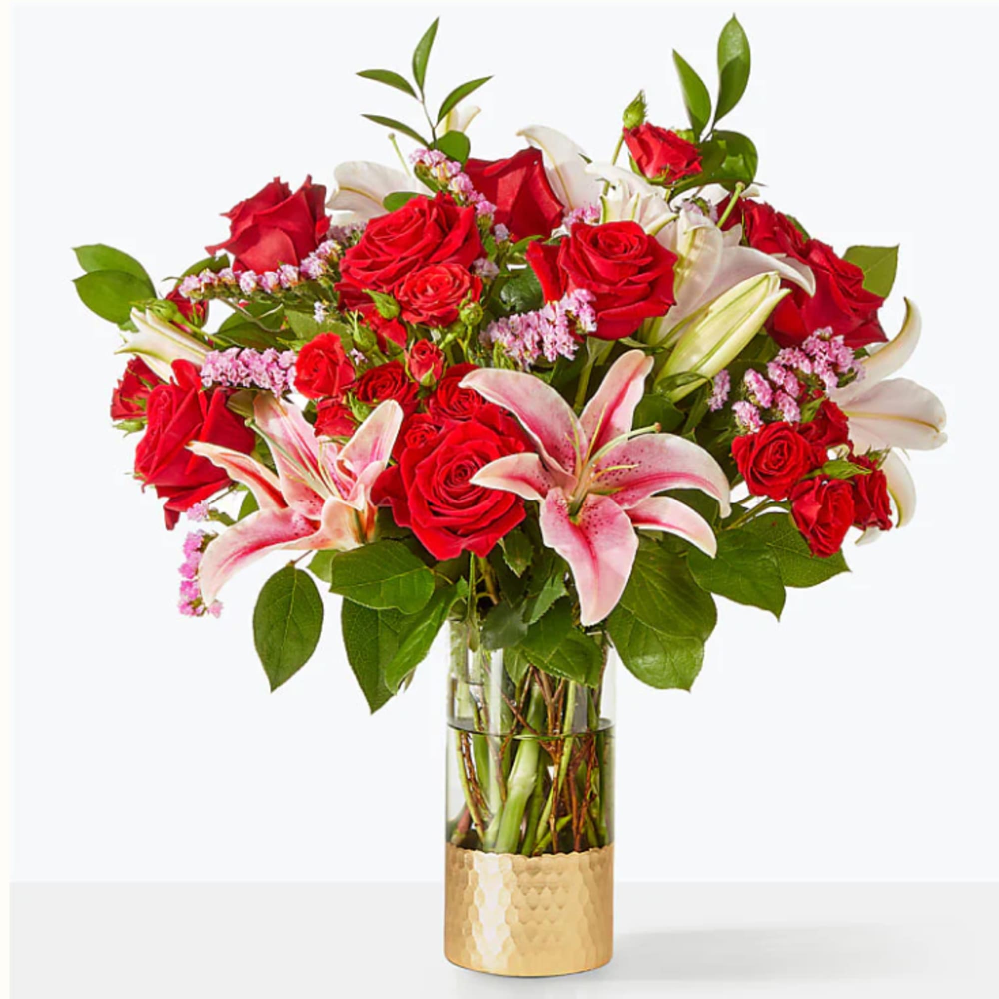Red roses and pink lilies in a clear glass vase with a gold base