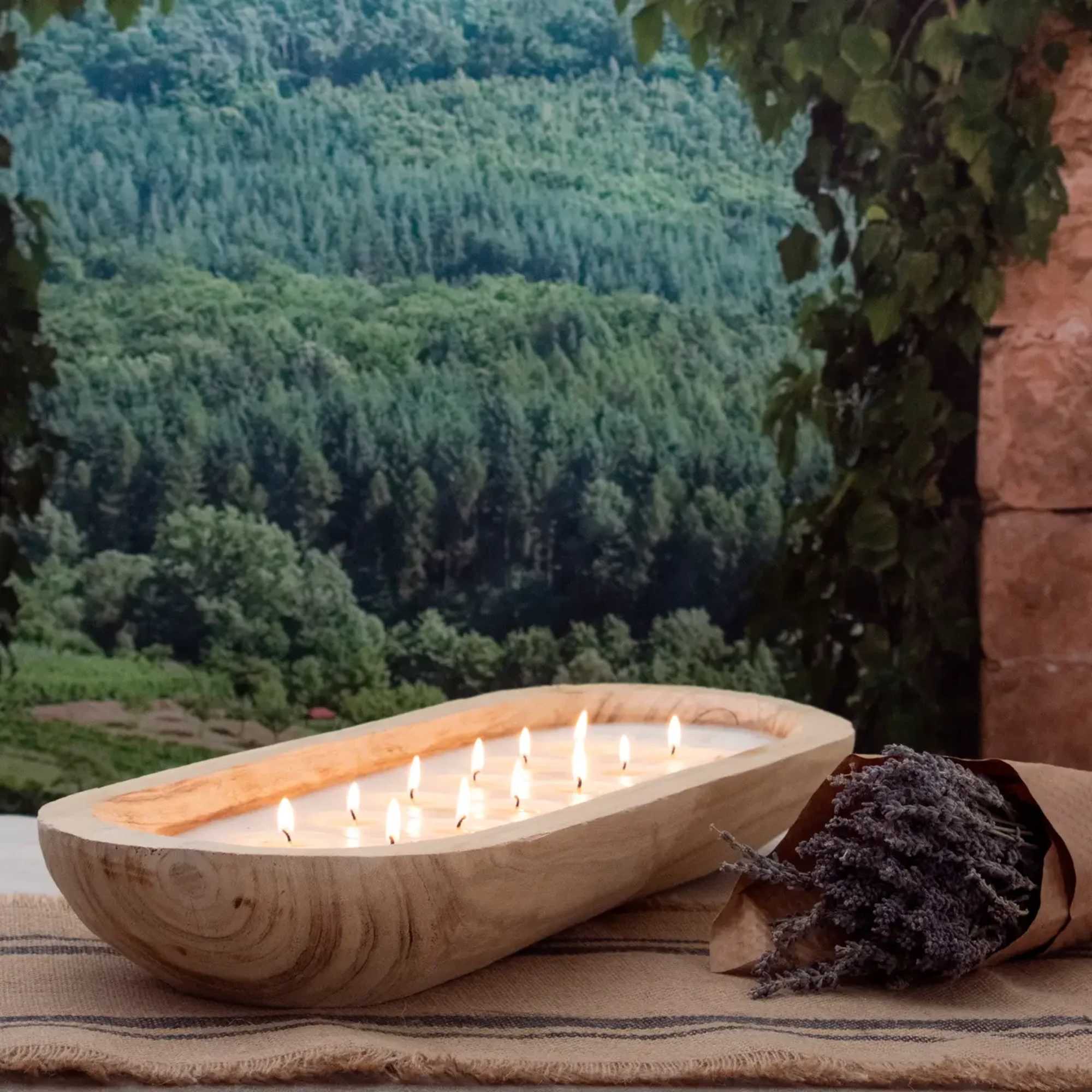 Wooden bowl candle with lit wicks beside a small dried lavender bouquet
