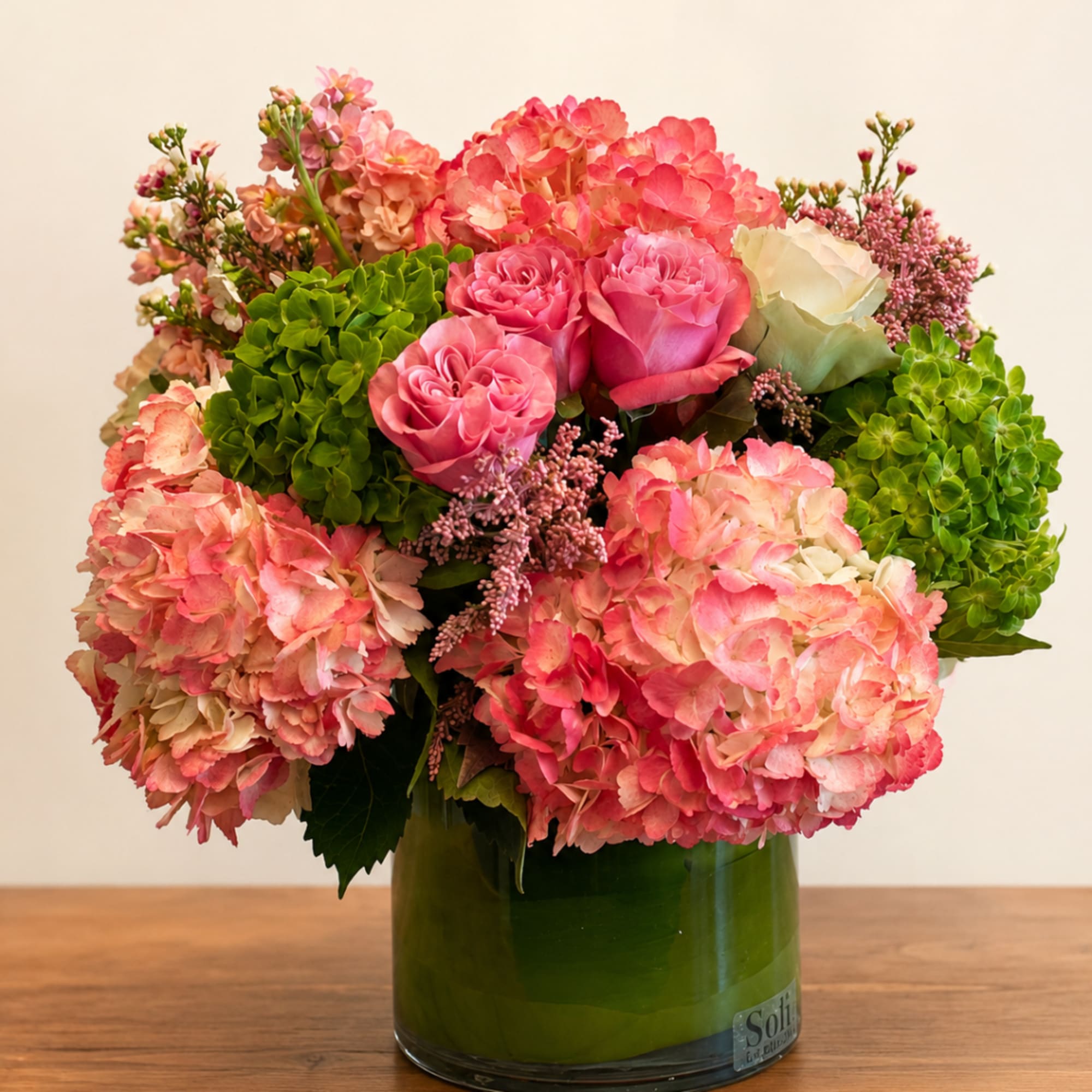 Pink hydrangeas and roses arranged in a green glass vase