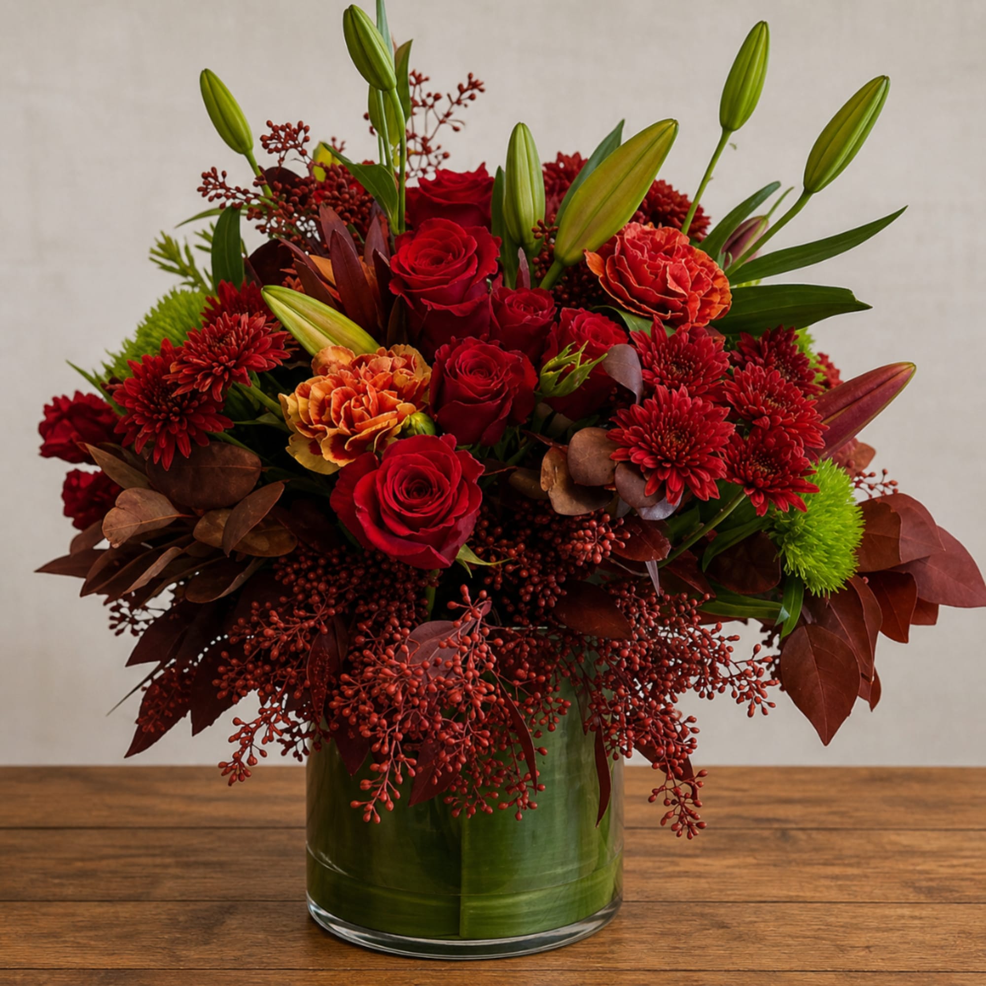 Red roses and lilies in a glass vase with burgundy accents
