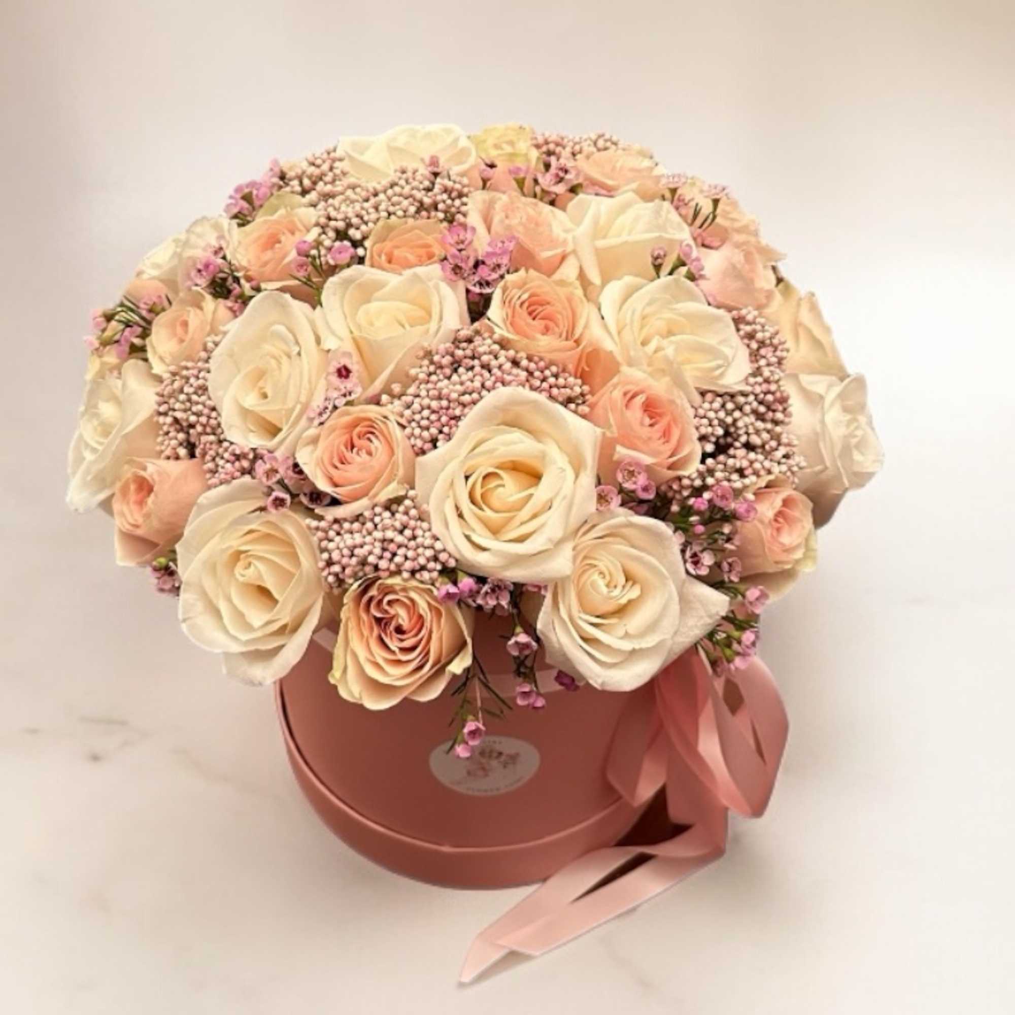 Cream and blush roses arranged in a pink round box with a ribbon