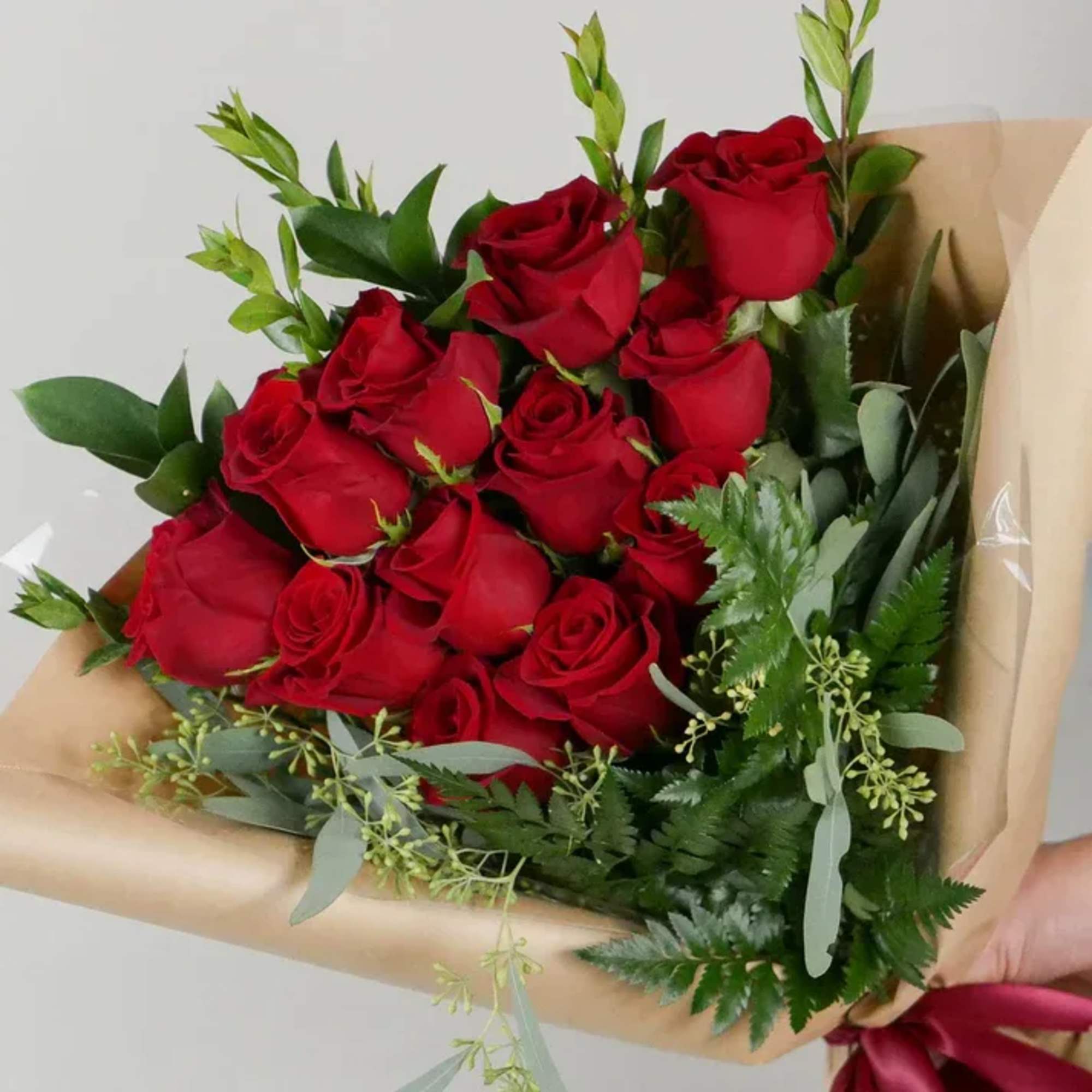 Bouquet of red roses wrapped in tan paper with greenery