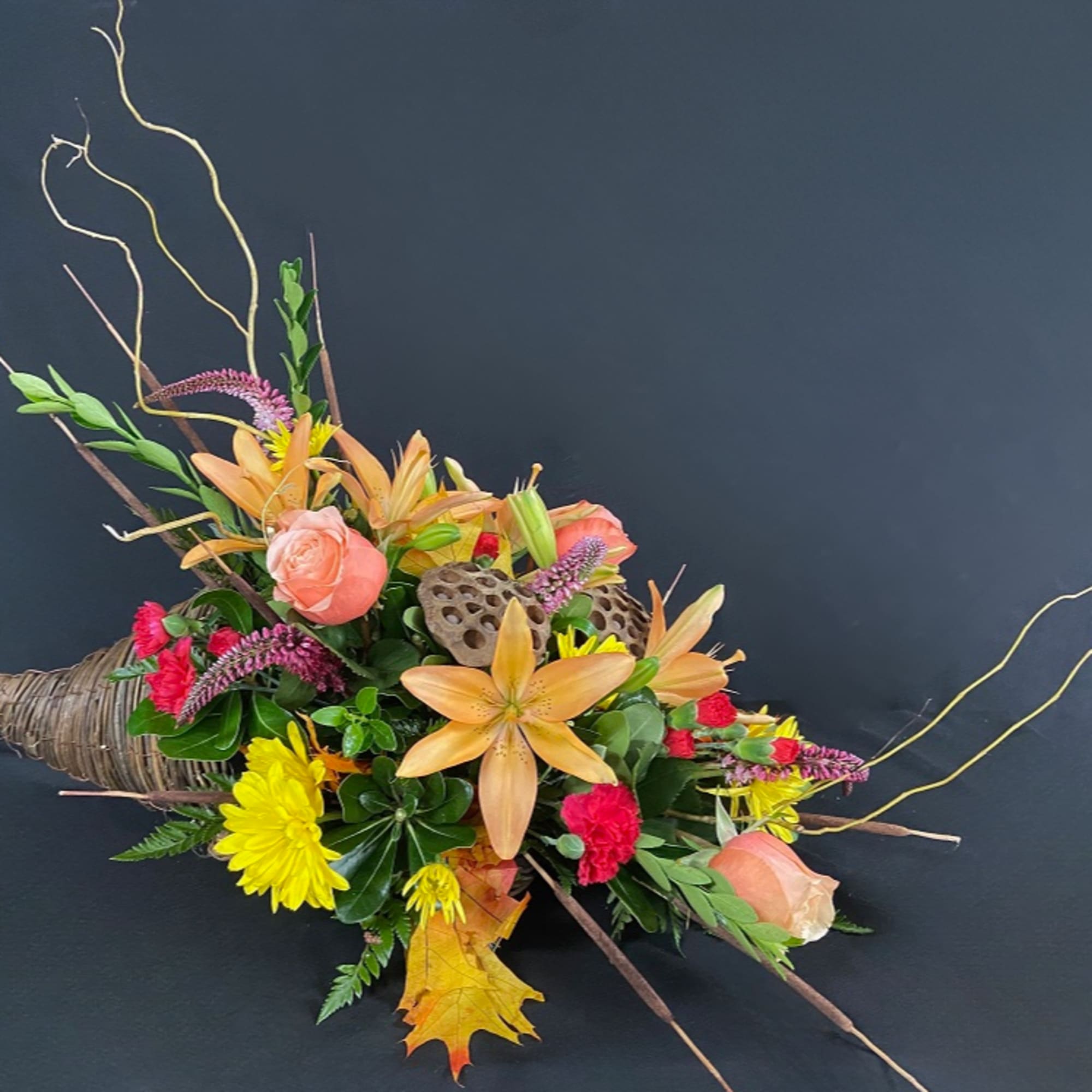 Mixed floral arrangement with peach lilies, roses, and yellow mums in a woven horn-shaped base