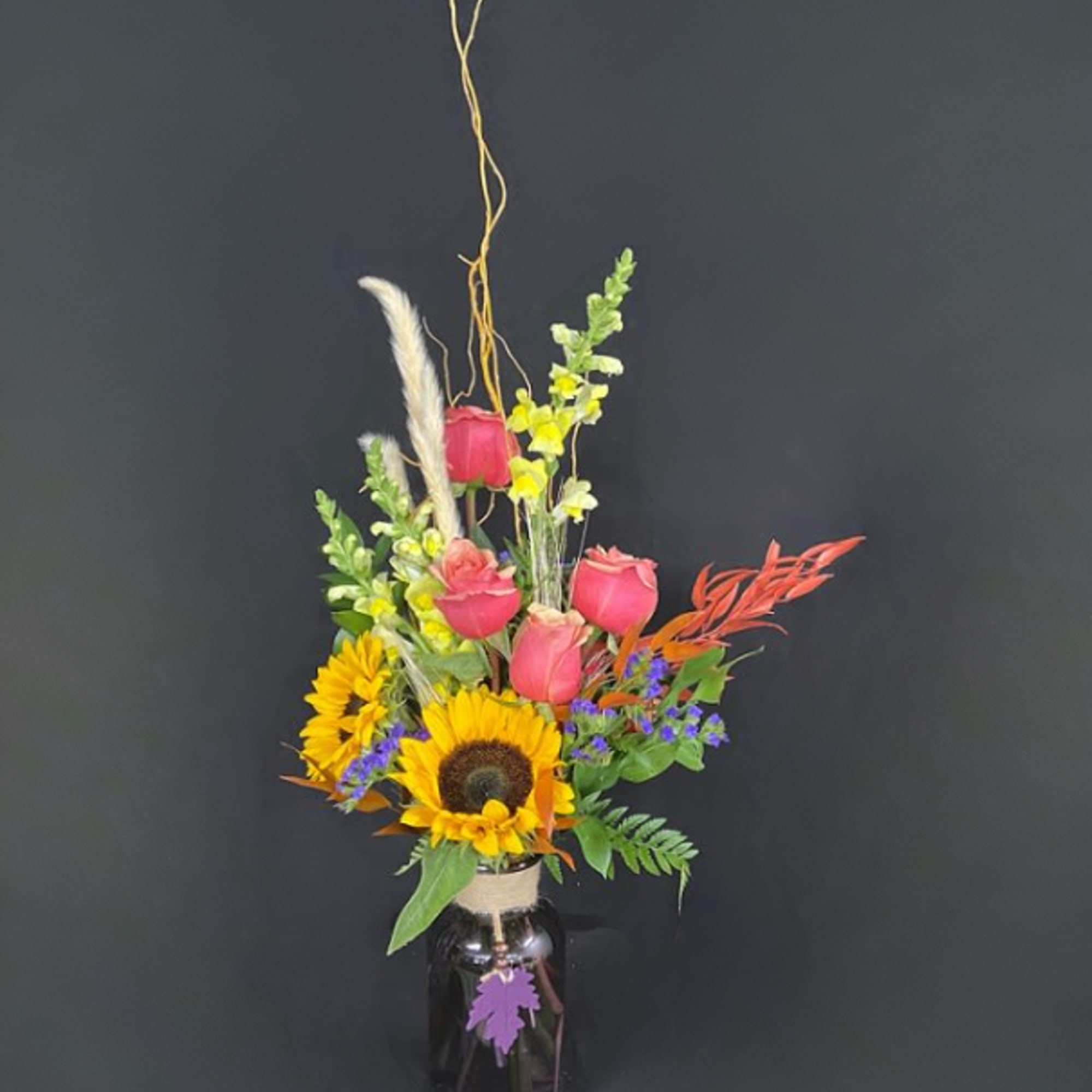 Tall bouquet of sunflowers and pink roses in a dark vase
