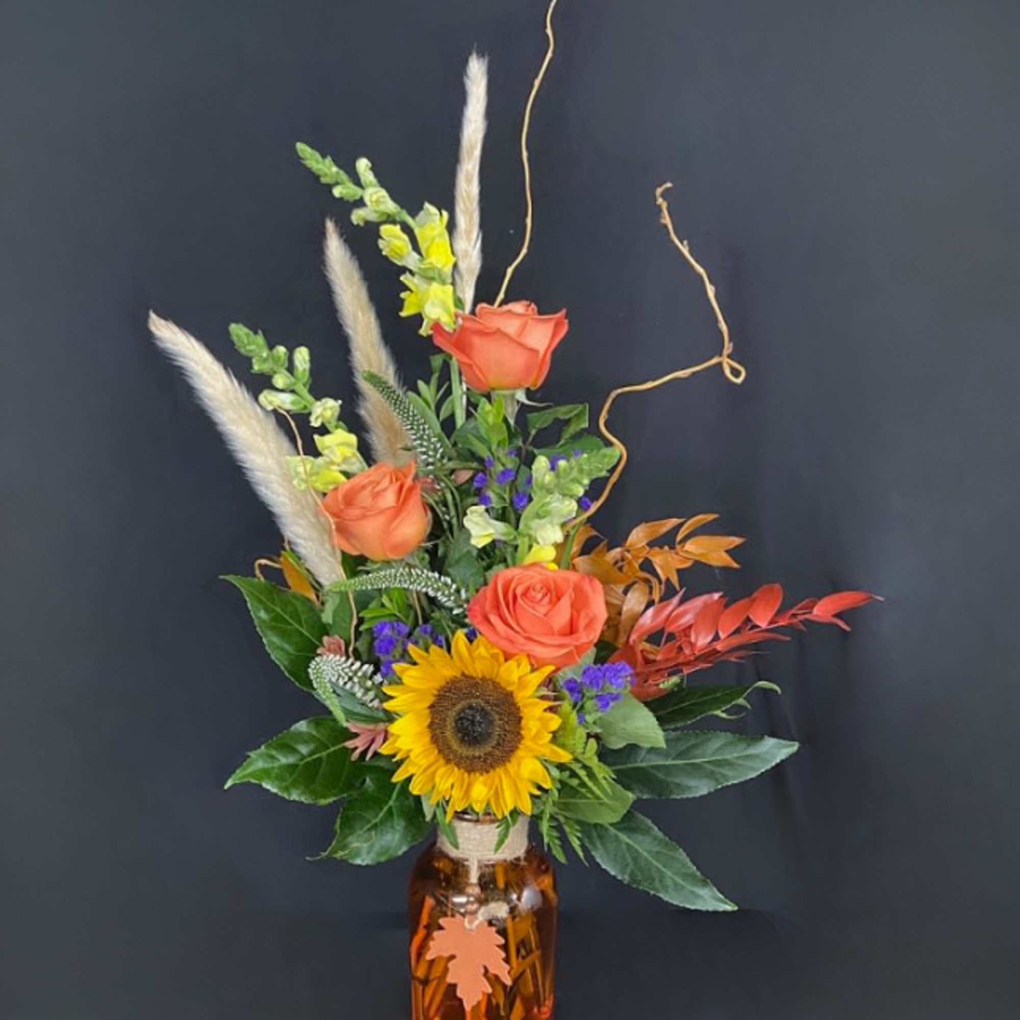 Sunflower and orange rose arrangement in an amber glass jar