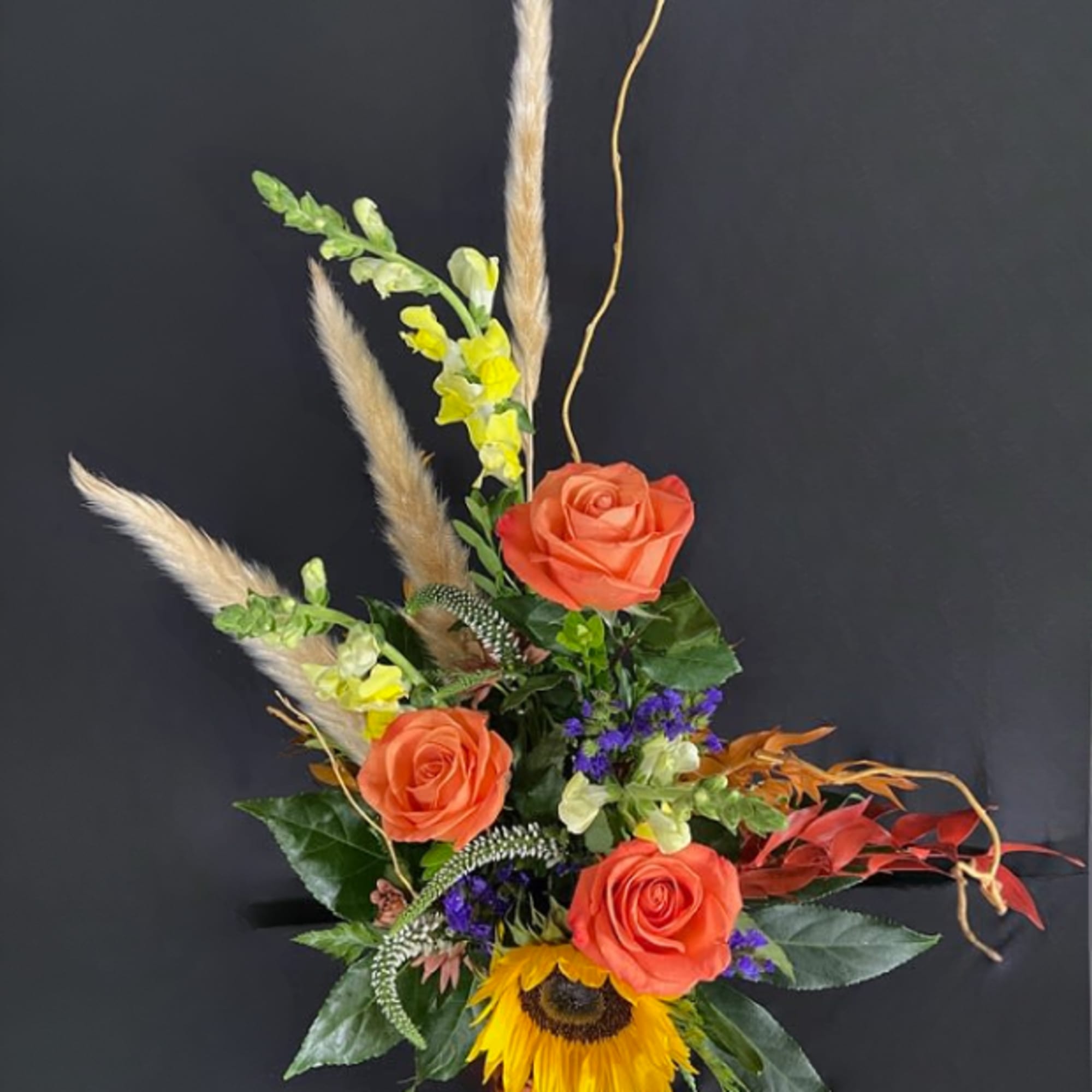 Orange roses and a sunflower in a glass vase with tall dried grasses