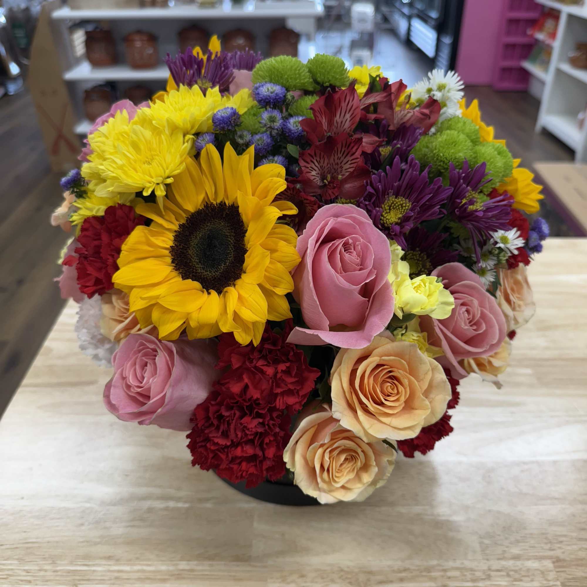 Mixed bouquet with sunflowers, pink roses, and purple blooms in a black vase