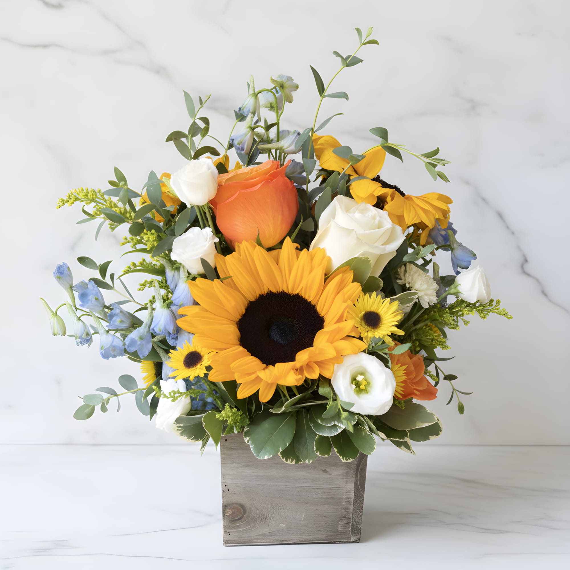 Sunflower bouquet with roses and blue flowers in a wooden box