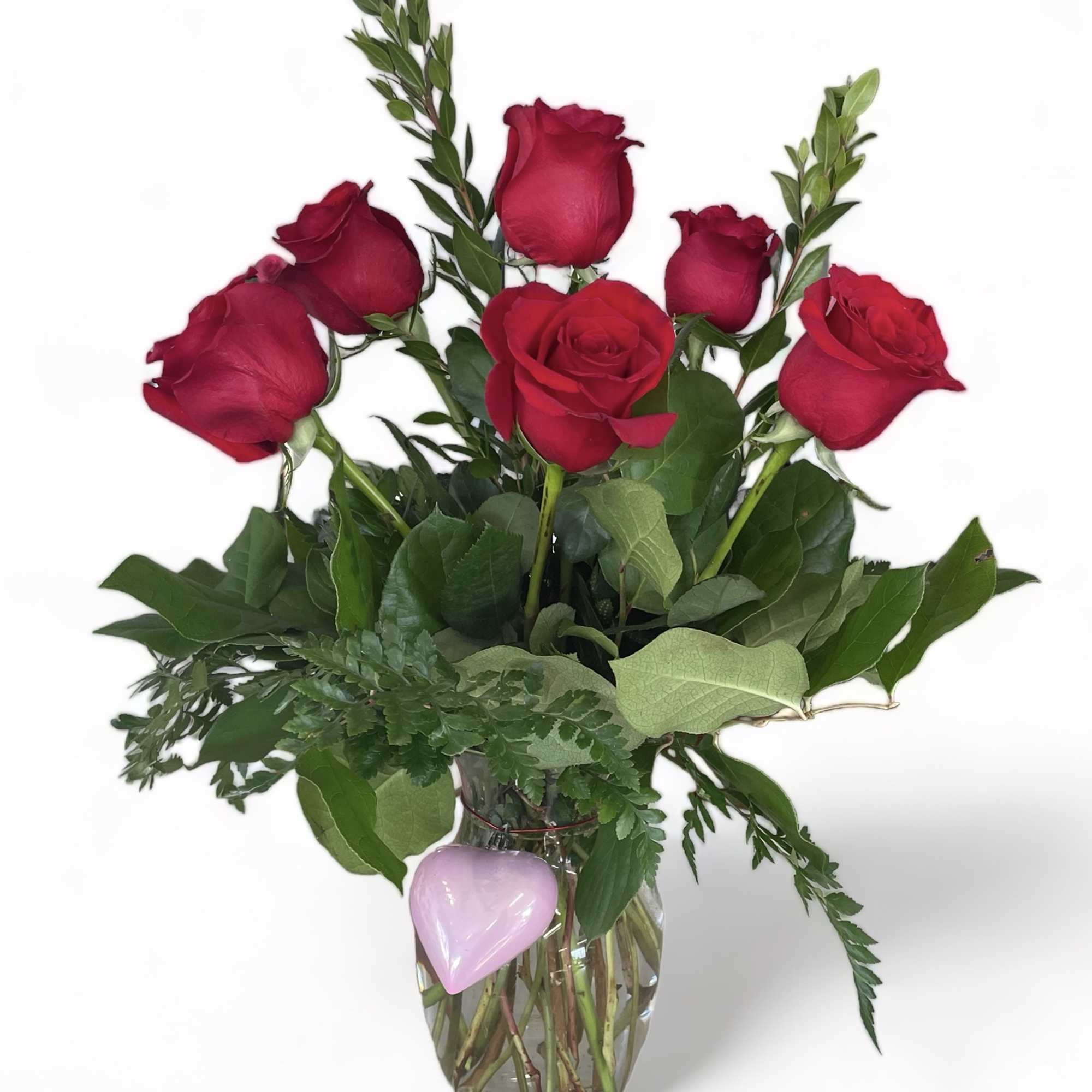 Red roses in a clear glass vase with a pink heart decoration