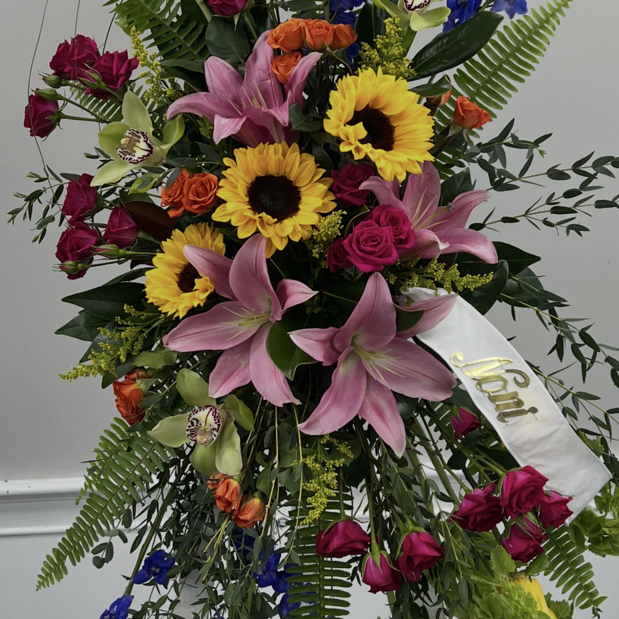 Tall standing floral spray with sunflowers, pink lilies, and blue delphinium
