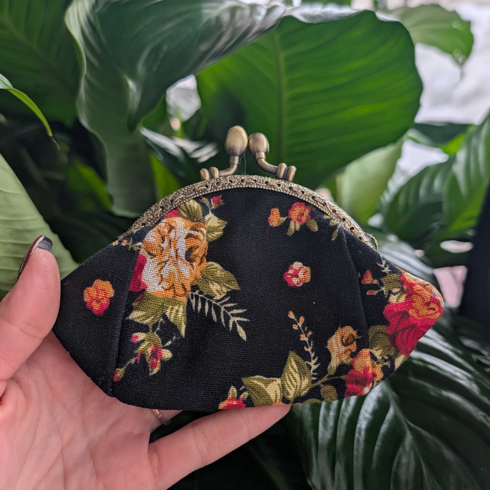 Floral-print fabric coin purse with a metal clasp held in a hand