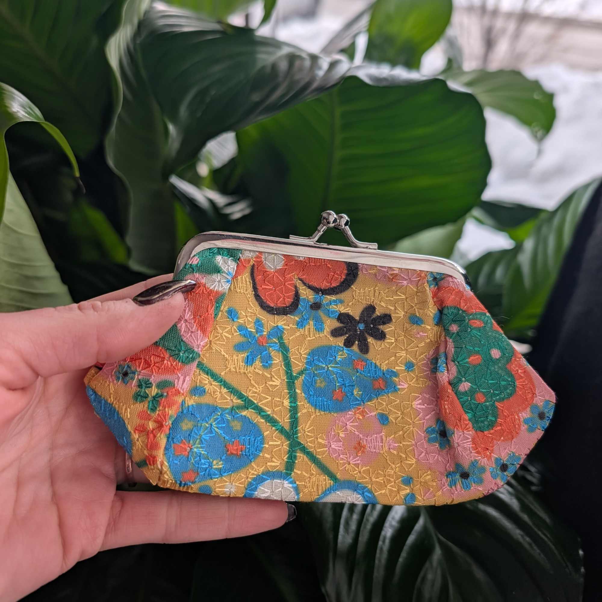 Colorful floral-pattern coin purse held in front of large green leaves