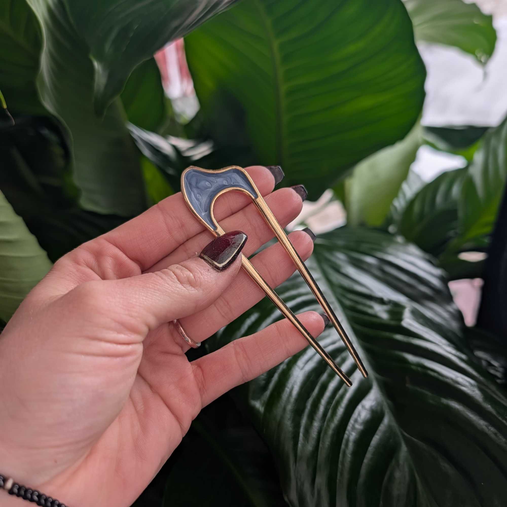 Hand holding a gold floral pick in front of large green leaves