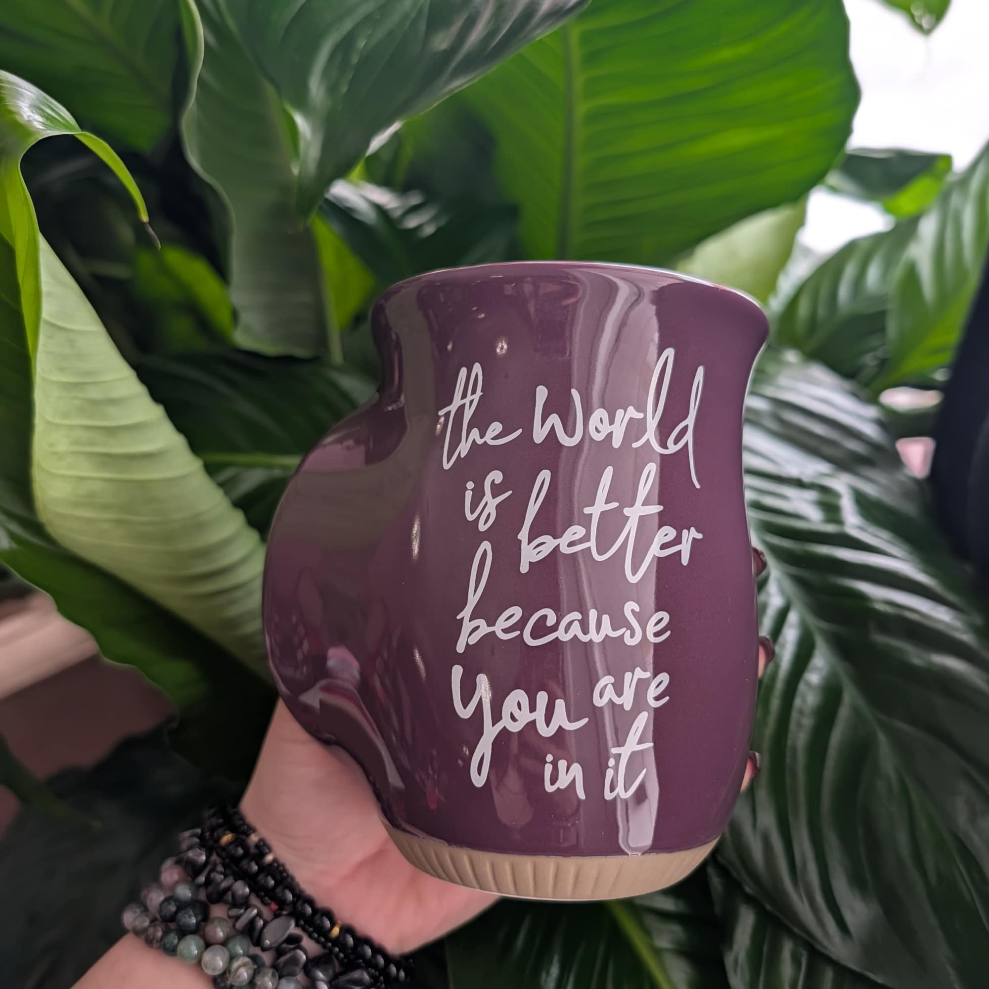 Purple ceramic planter with white text held in front of large green leaves