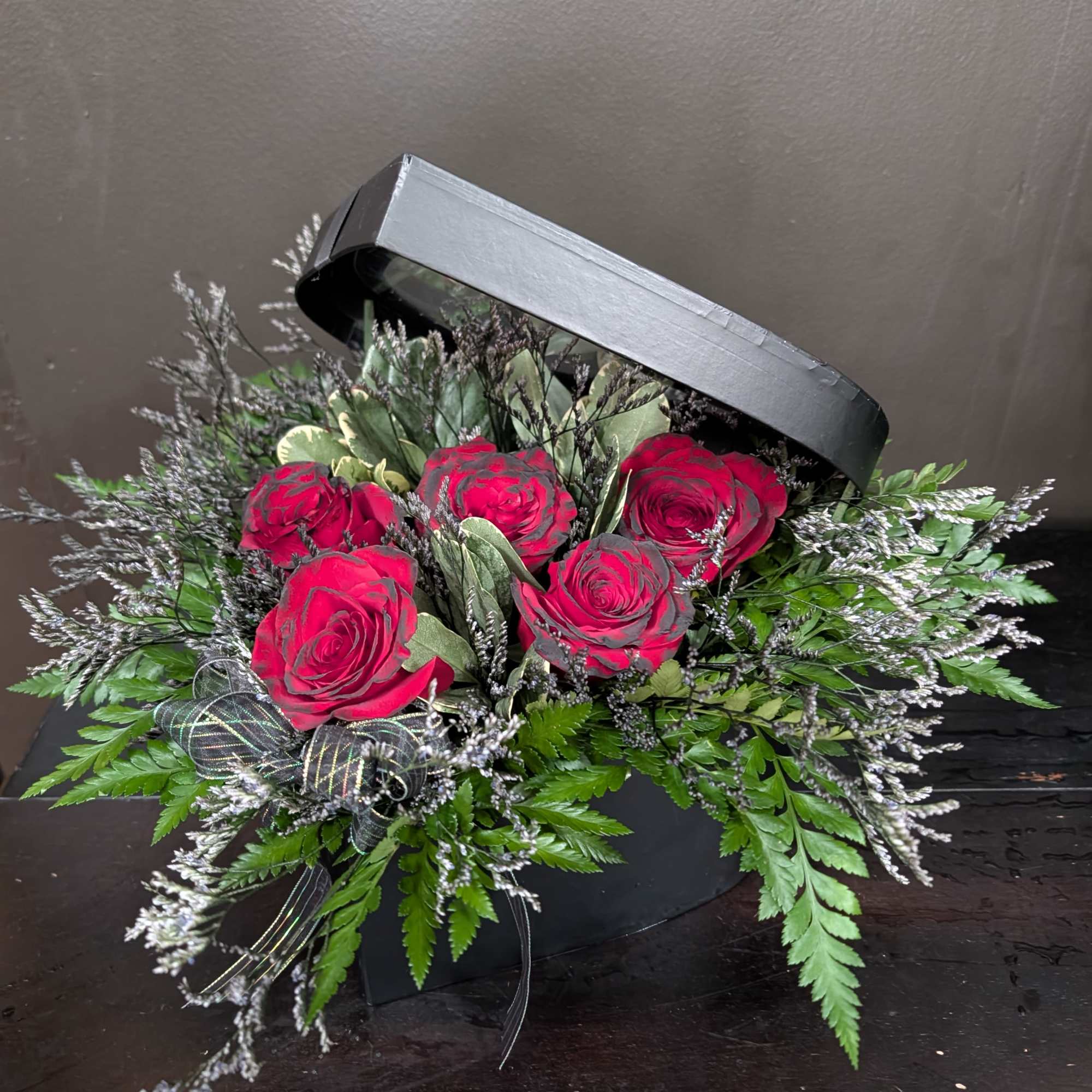 Red roses in a black hatbox with greenery and ribbon