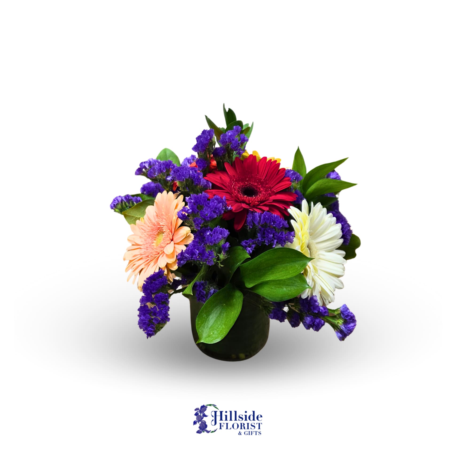 Short glass vase of red, peach, and white gerbera daisies with purple filler flowers.