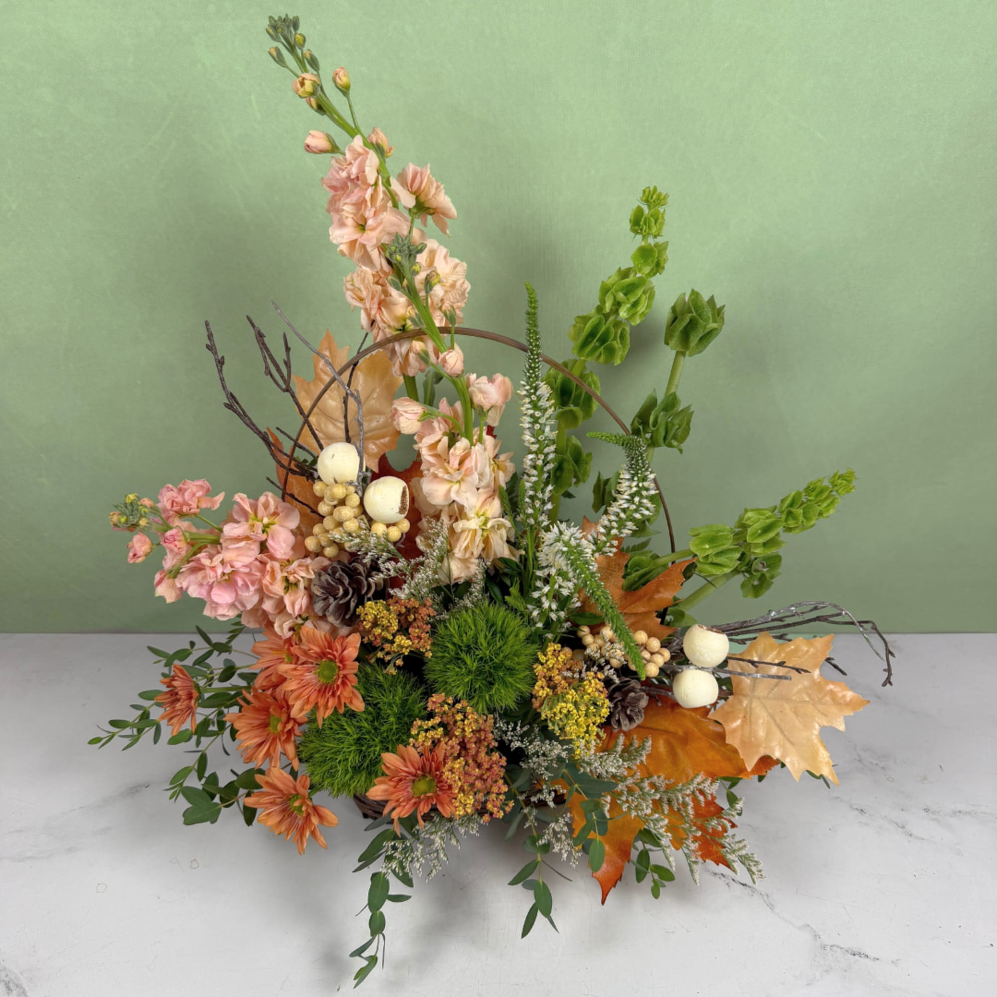 Autumn floral arrangement with peach blooms and orange daisies in a low container