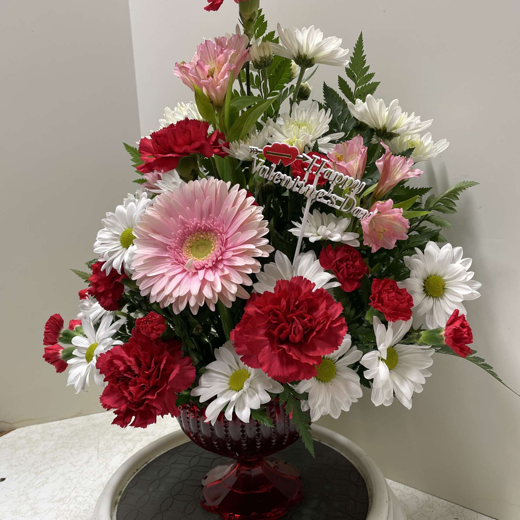 Pink and red flowers arranged in a red glass vase with a Valentine’s Day pick