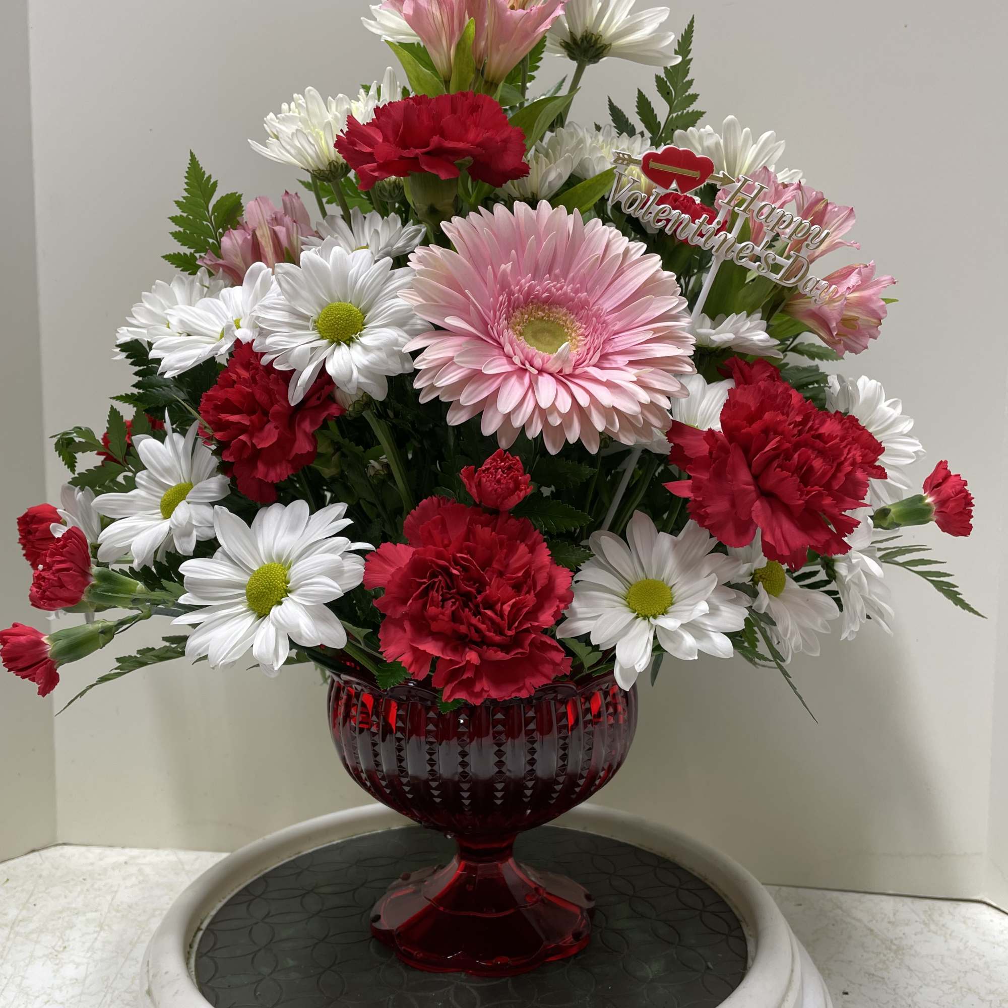 Red and pink flowers arranged in a red glass vase with a Valentine sign