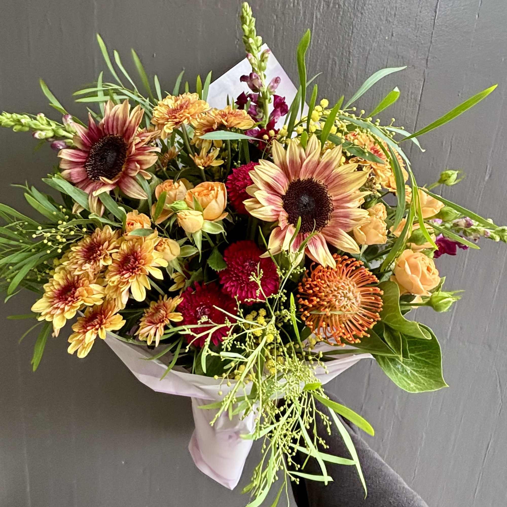 Mixed bouquet with sunflowers, roses, and chrysanthemums wrapped in pale paper