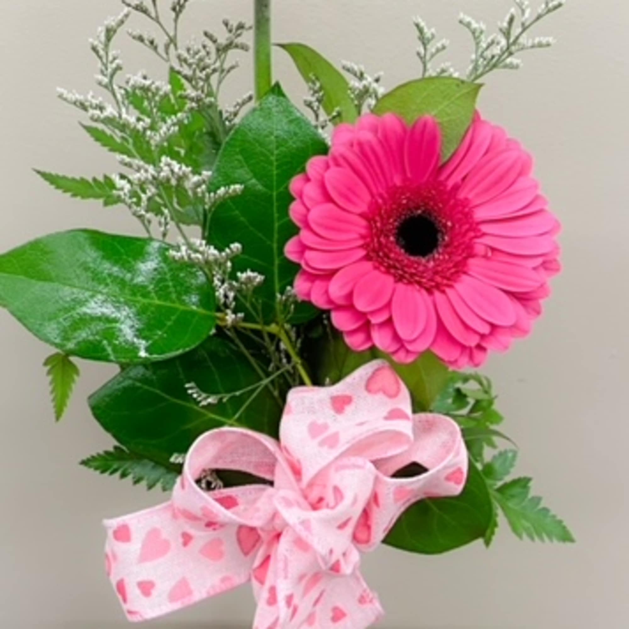 Two pink gerbera daisies in a clear vase with a pink heart ribbon