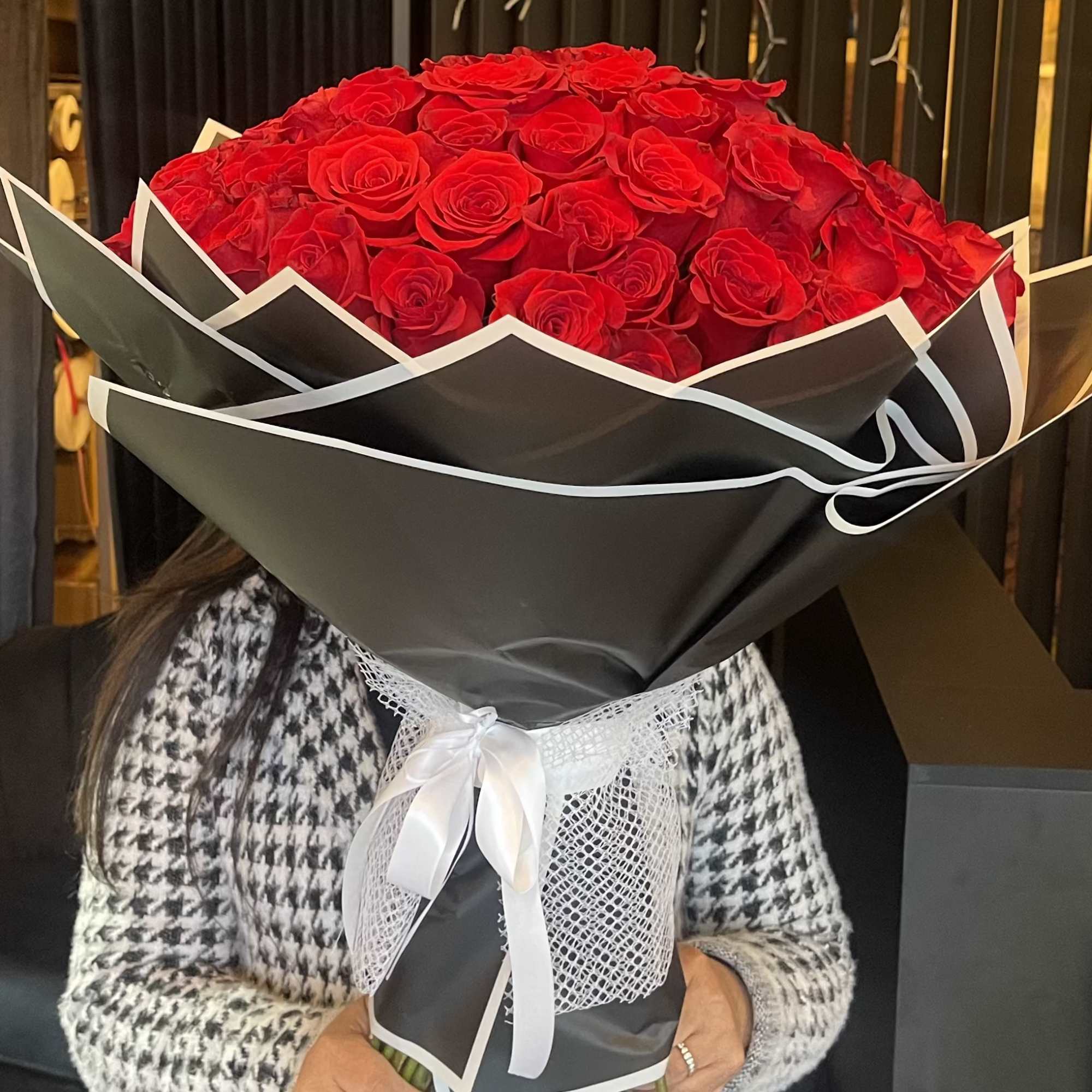 Large bouquet of red roses wrapped in black paper with a white ribbon