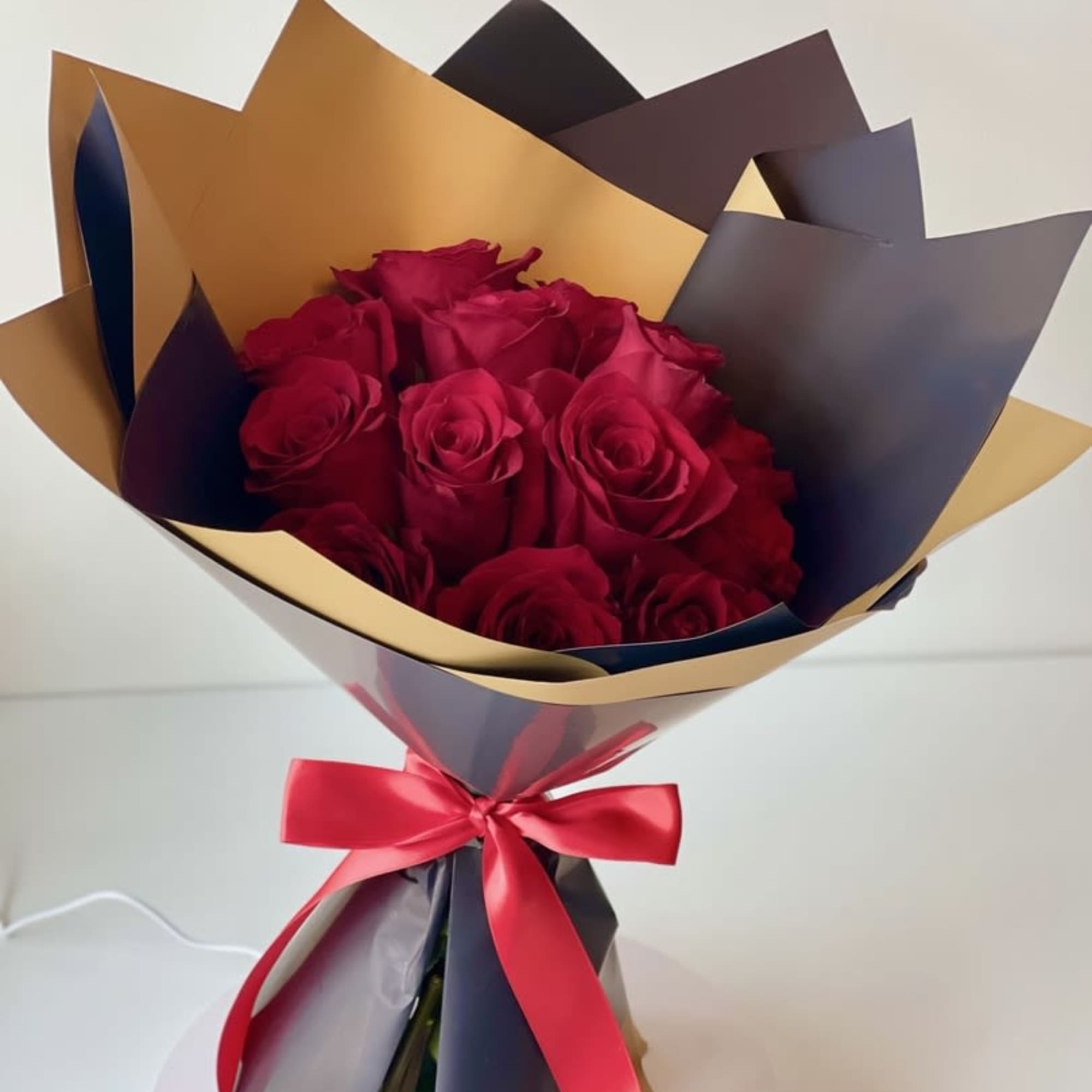 Bouquet of red roses wrapped in gold and dark paper with a red ribbon