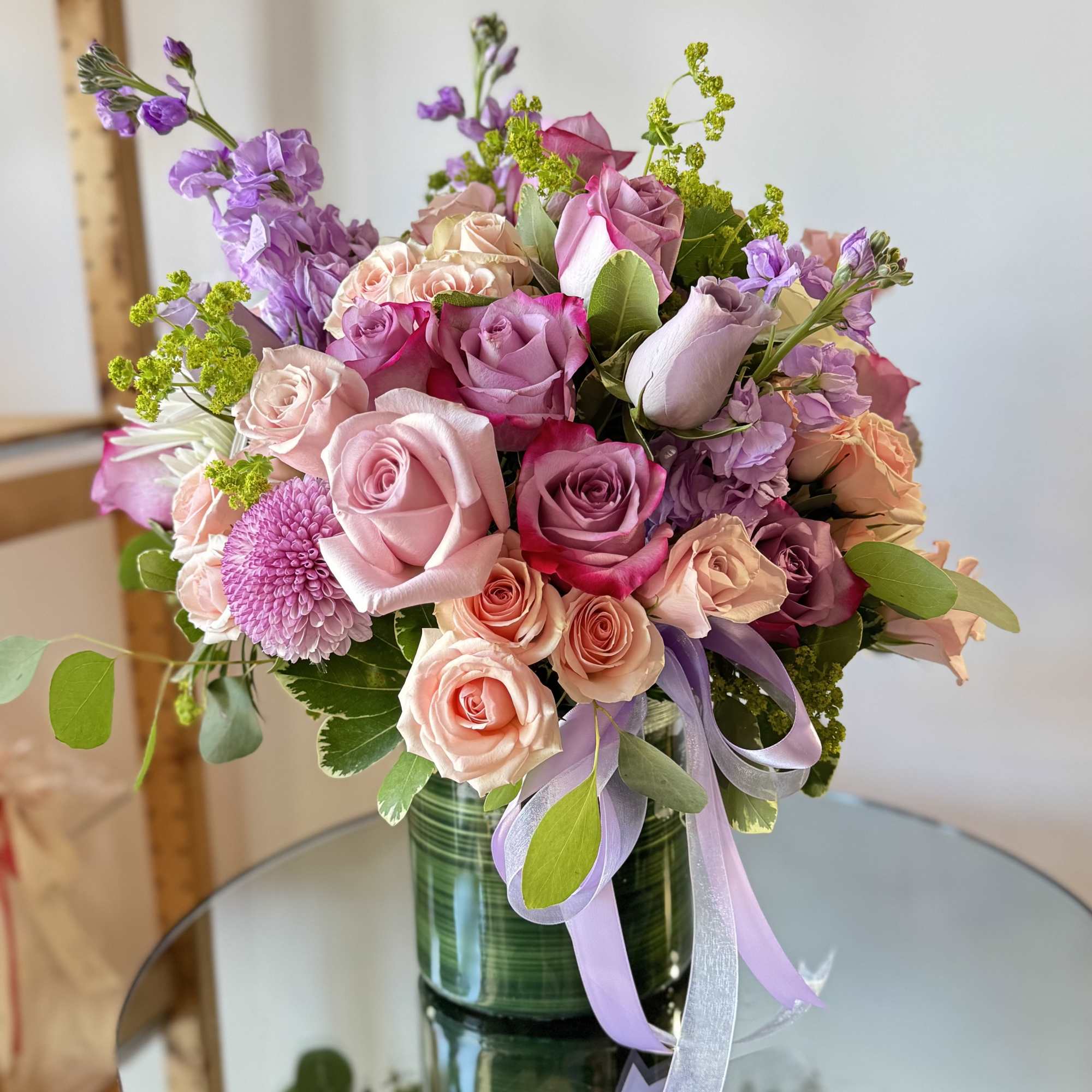 Pink and lavender rose bouquet in a green glass vase with ribbon