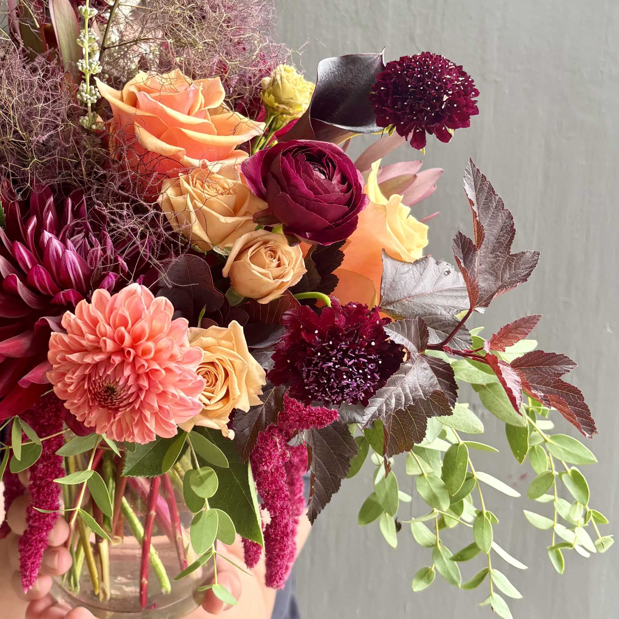Mixed bouquet of roses, dahlias, and dark burgundy blooms in a glass vase