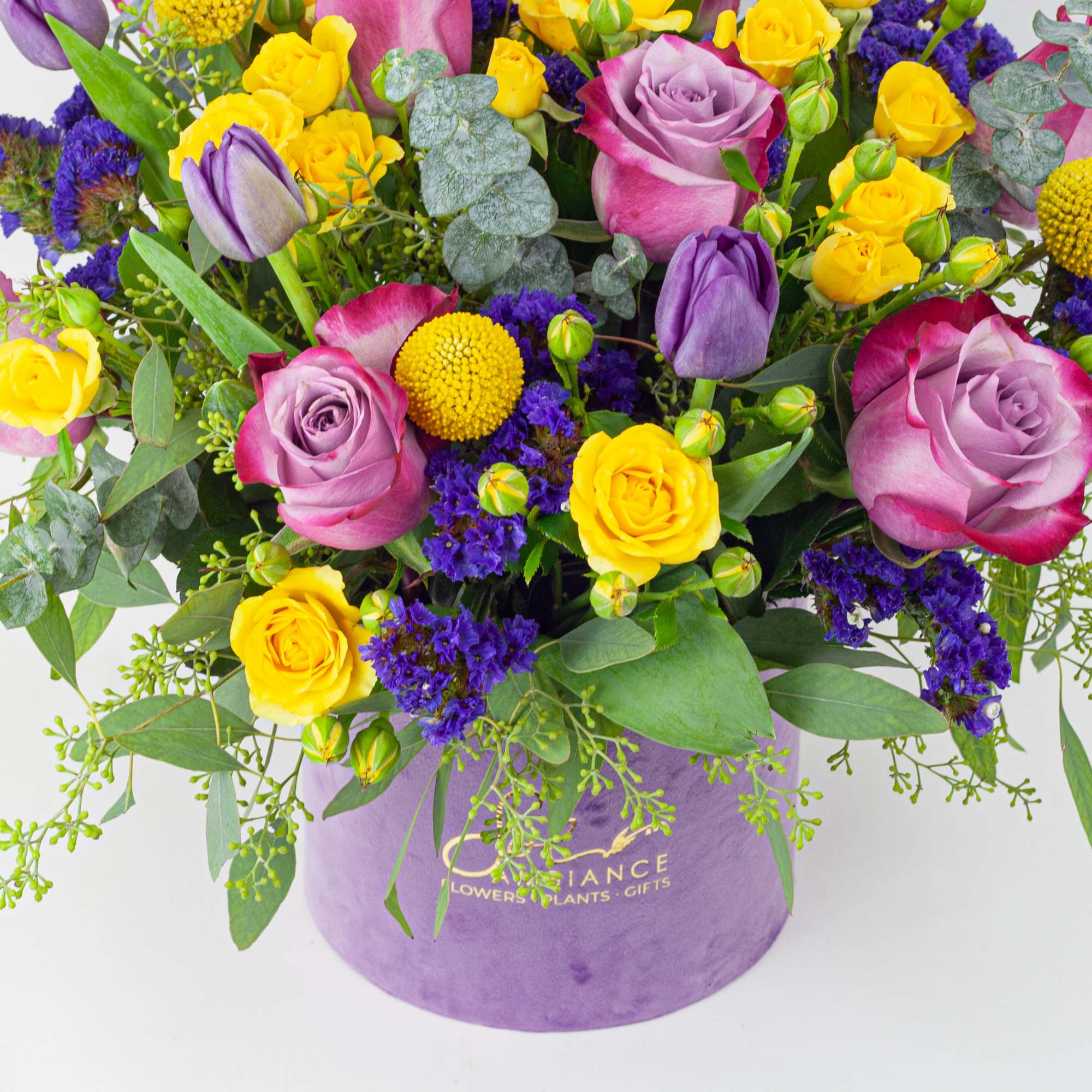 Bouquet of pink and yellow roses with purple accents in a lavender box