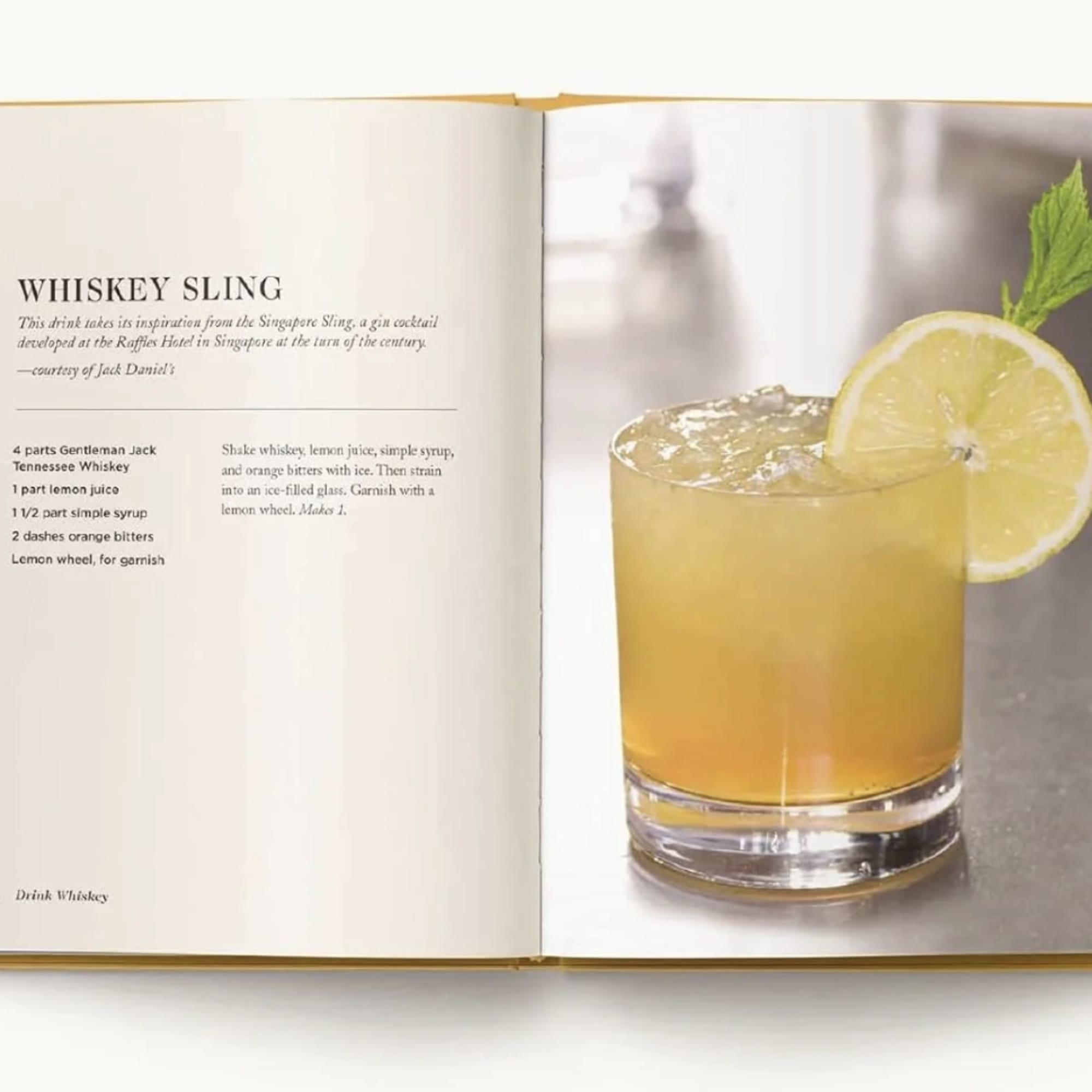 Open cookbook showing a whiskey cocktail recipe and a lemon-garnished drink