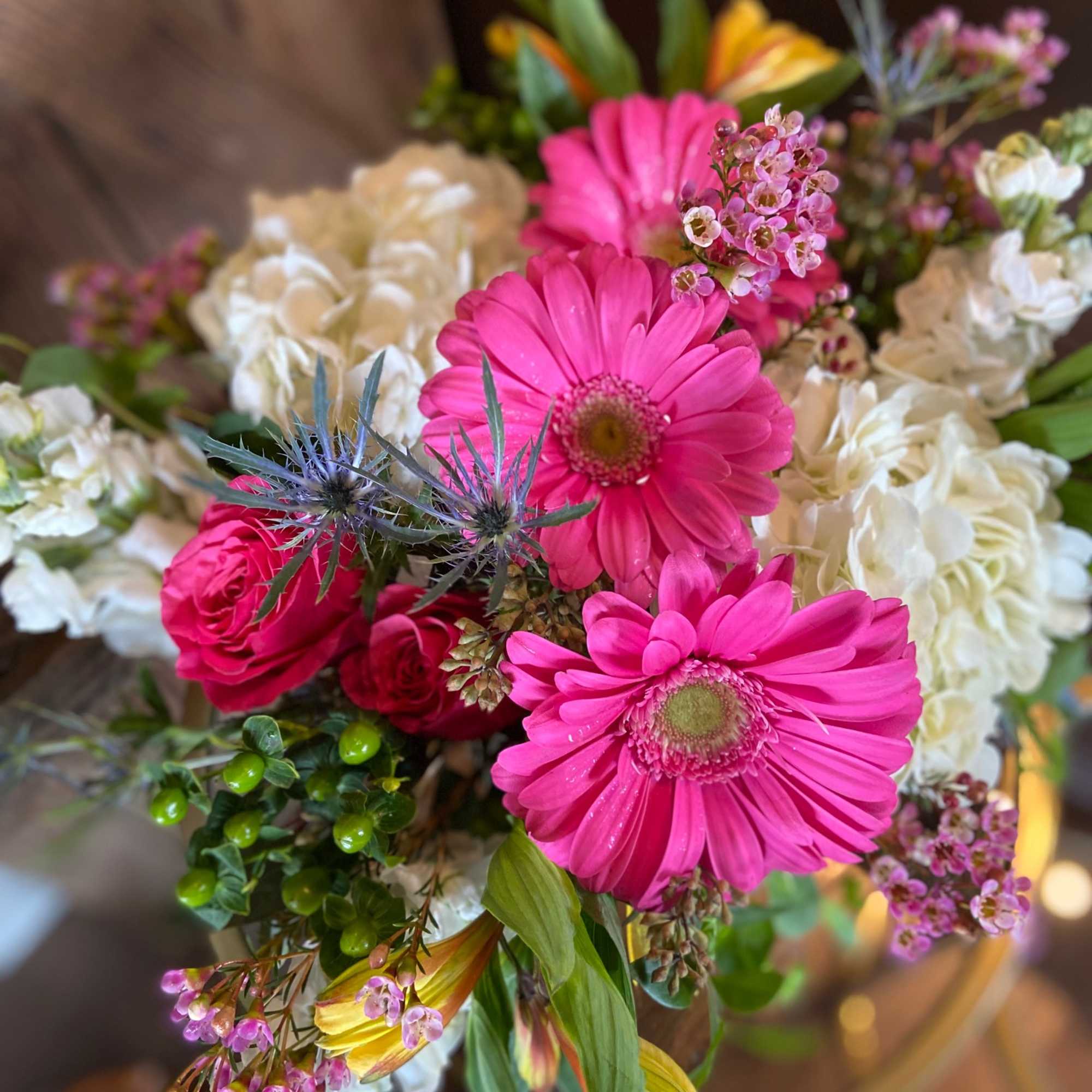 Bright bouquet with hot pink gerbera daisies, pink roses, white hydrangeas, and yellow alstroemeria in a glass vase