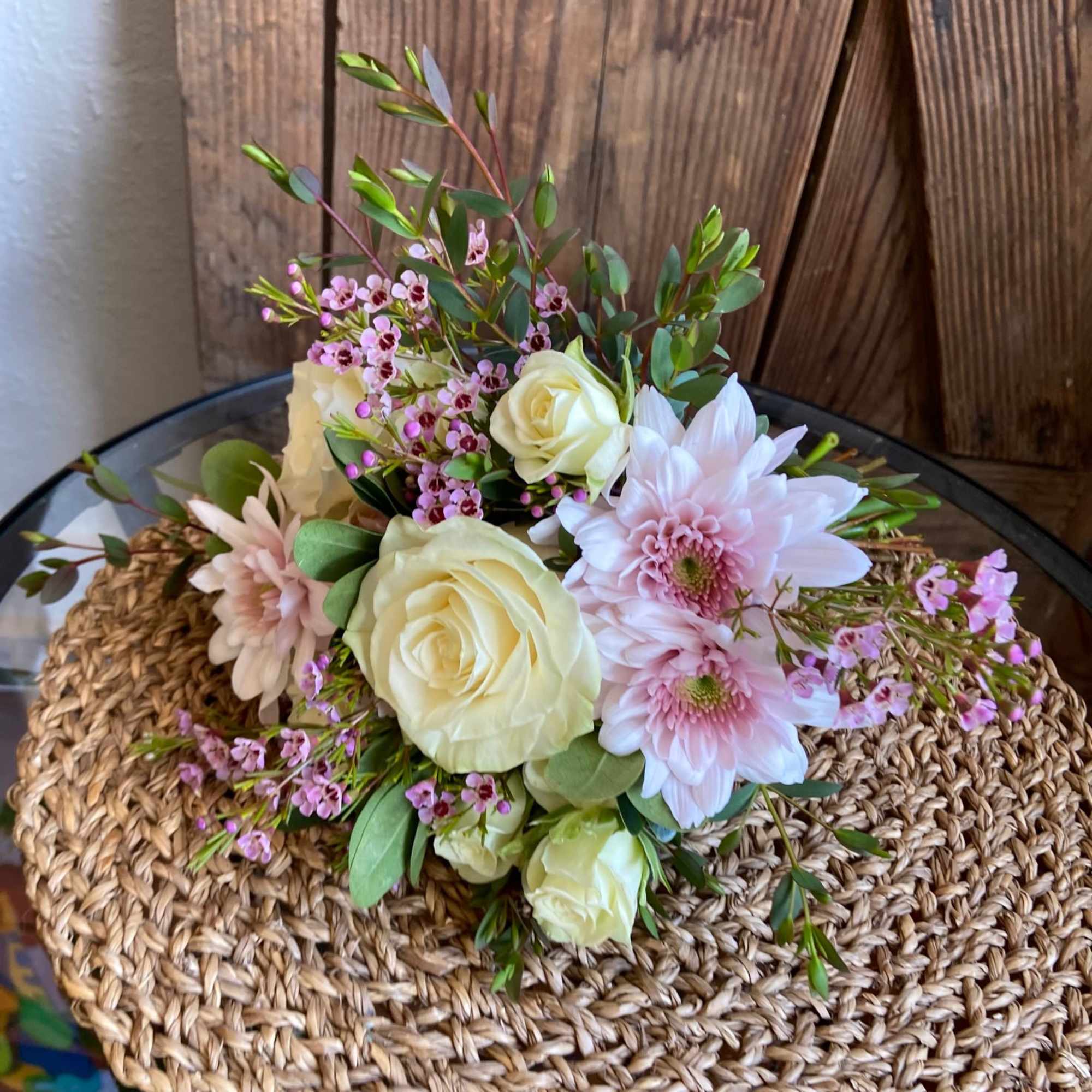 Low arrangement of cream roses and pale pink mums with tiny pink blossoms on a woven mat