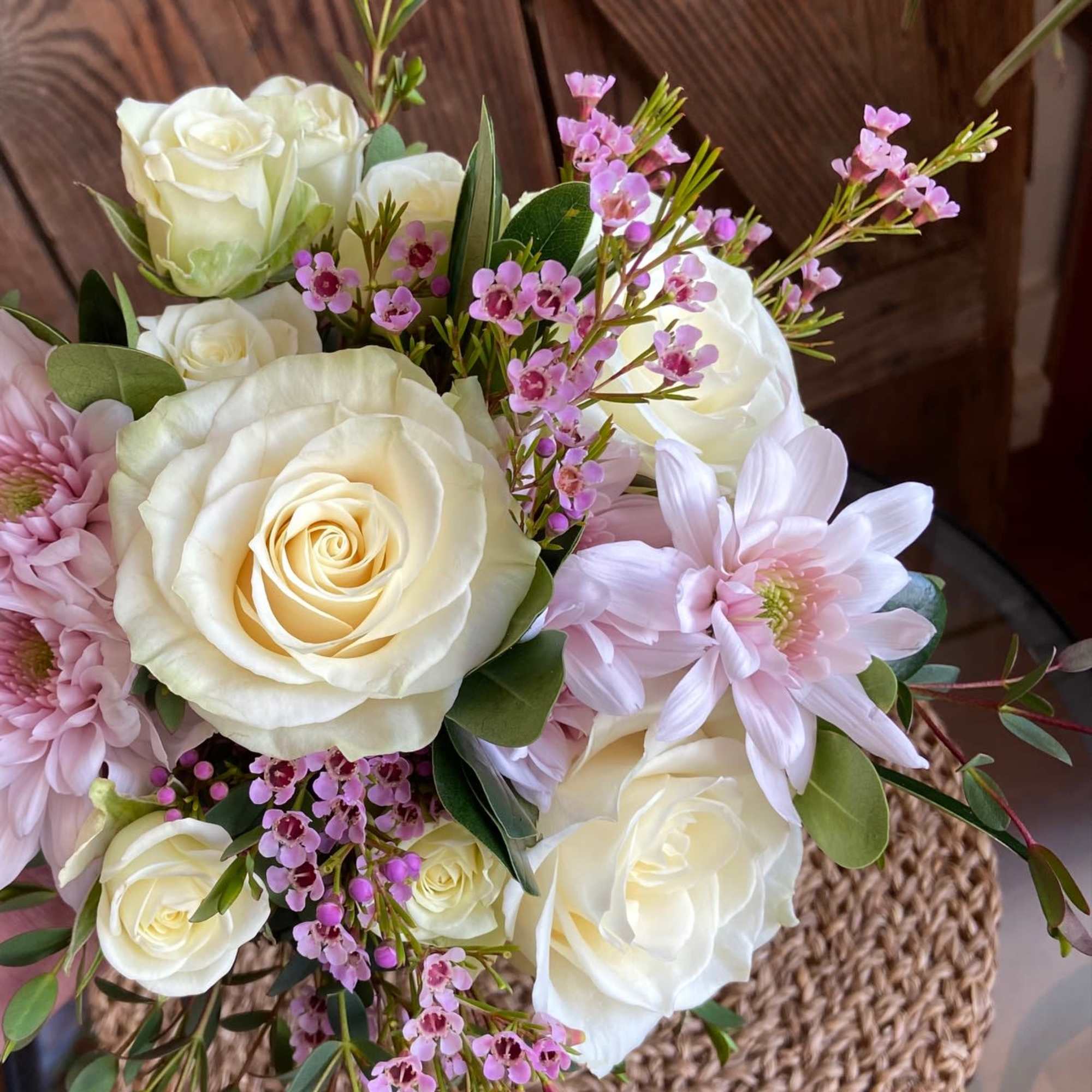 Pastel arrangement of white roses and pale pink mums with tiny pink blossoms in a glass vase