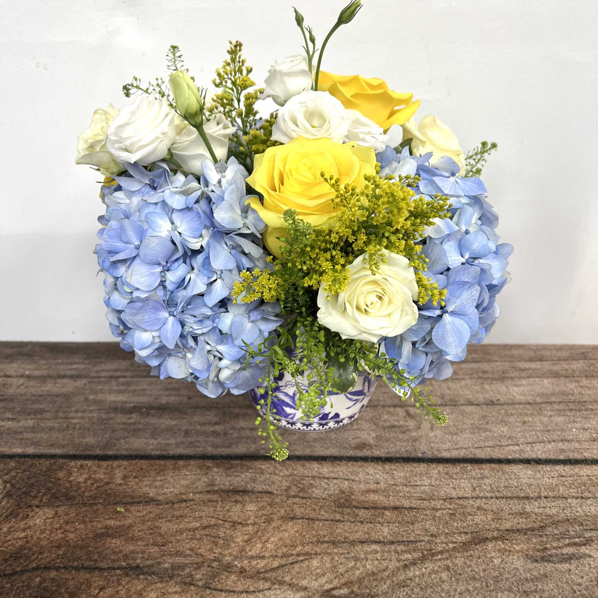 Blue hydrangeas with yellow and white roses in a small vase