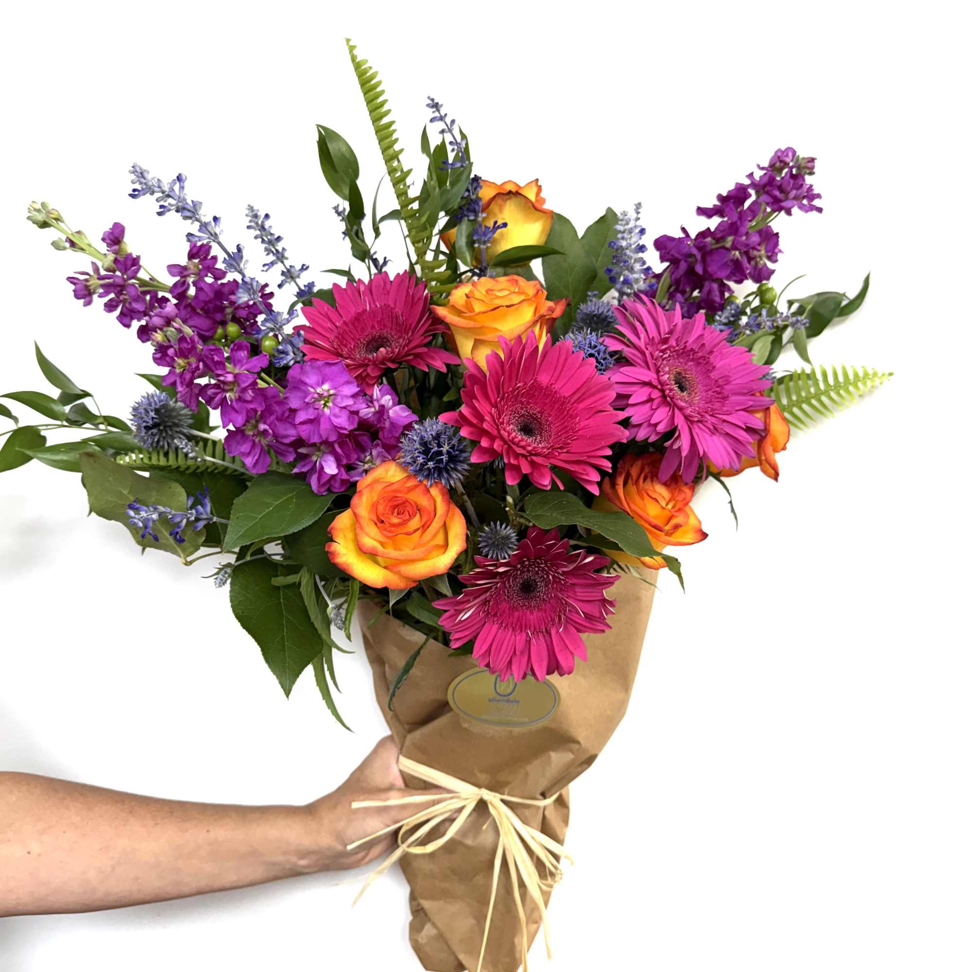 Bright mixed bouquet of orange roses, pink gerberas, and purple blooms in brown paper