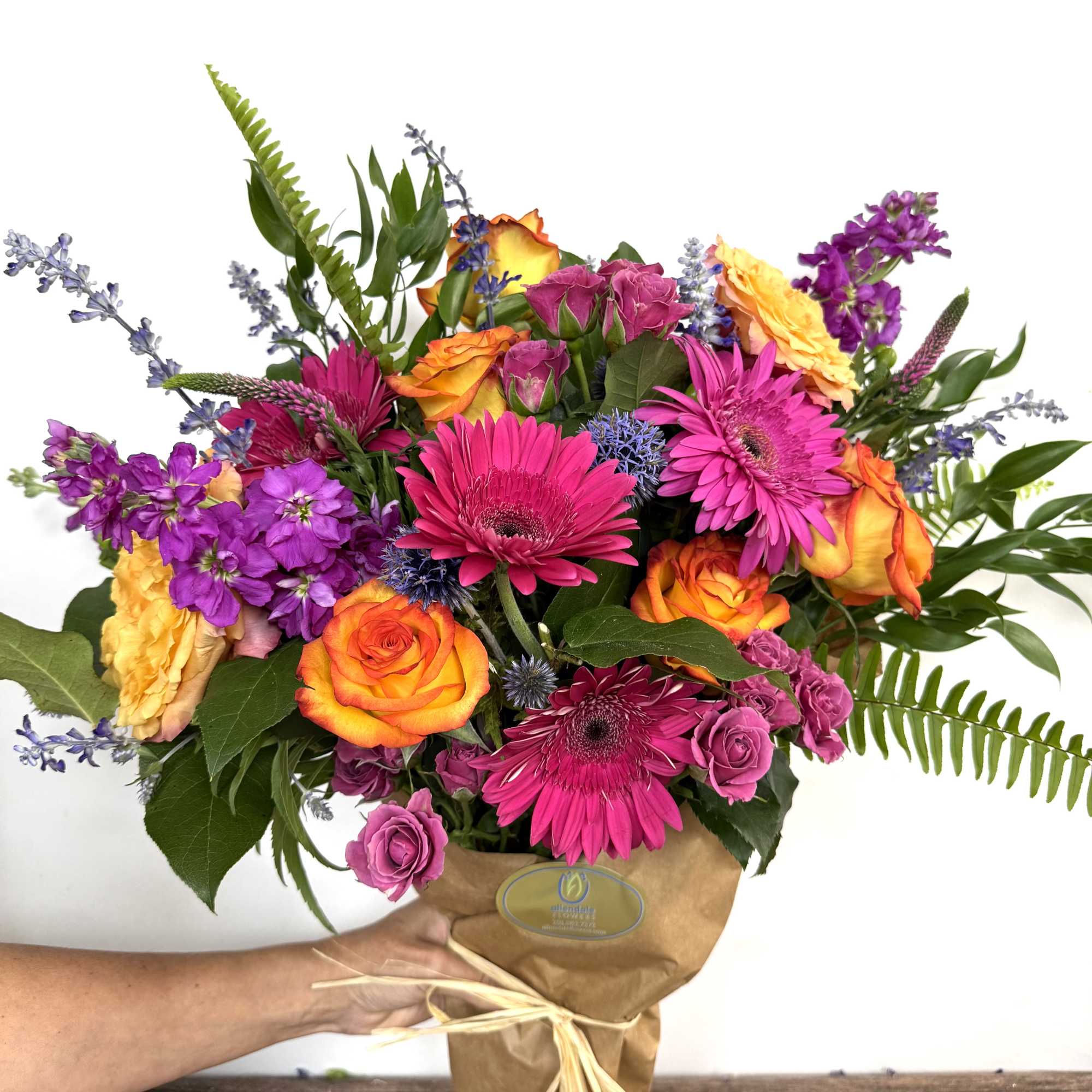 Mixed bouquet of pink, orange, and purple flowers wrapped in brown paper