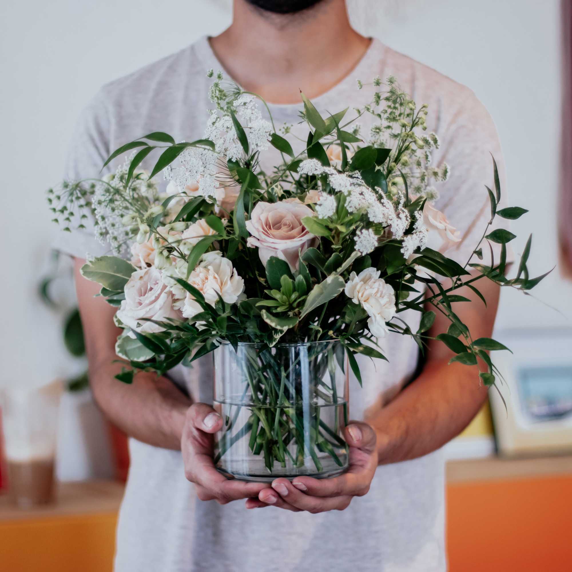 Person holding a glass vase of pale pink roses and white filler flowers