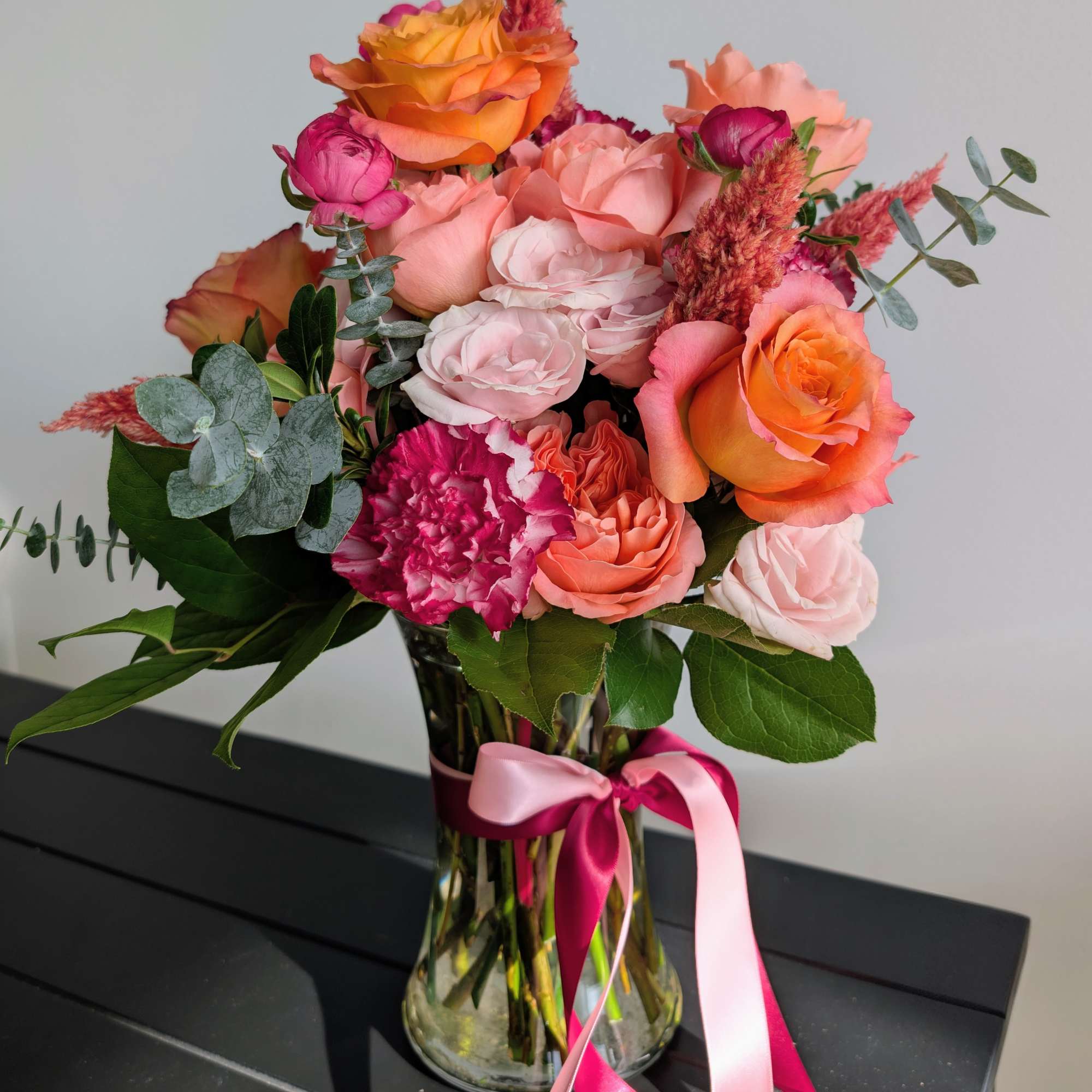 Bouquet of pink and orange roses in a glass vase with a pink ribbon