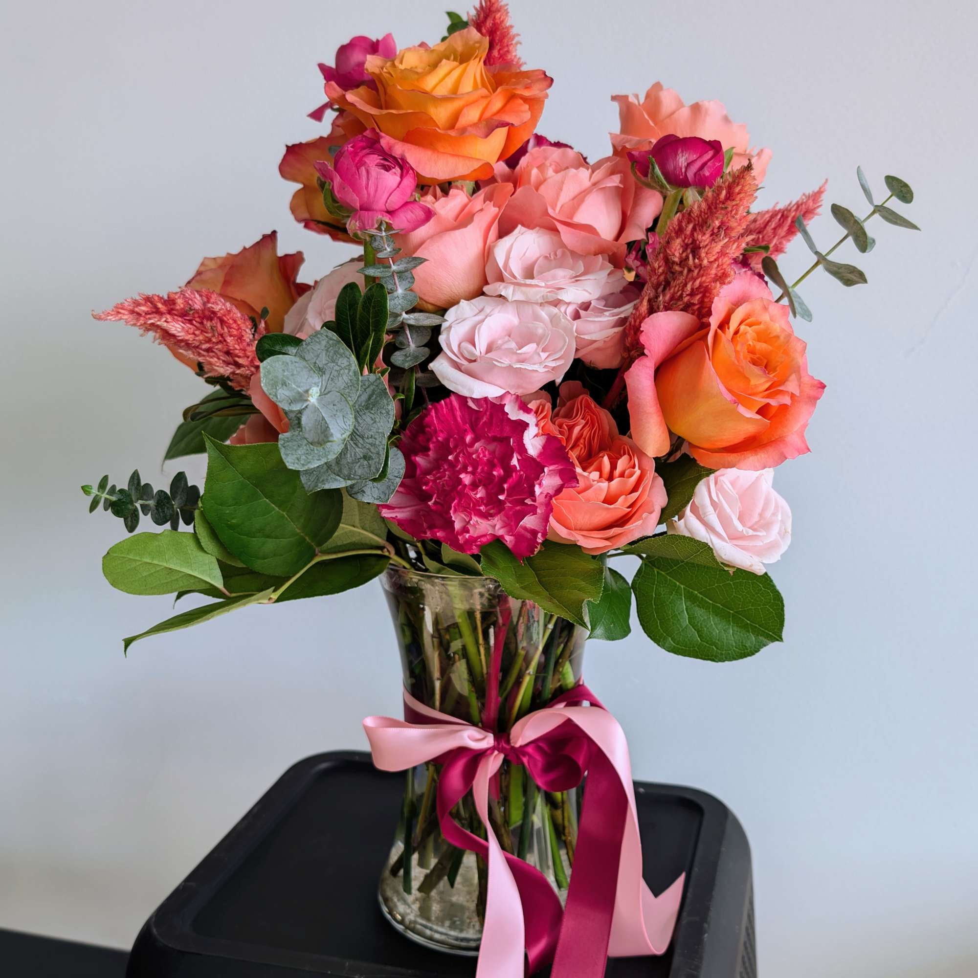 Bouquet of orange and pink roses in a glass vase with ribbon